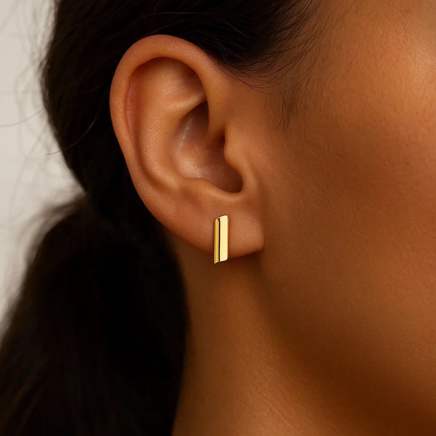 14k yellow gold polished rectangular post earrings on a person's ear.