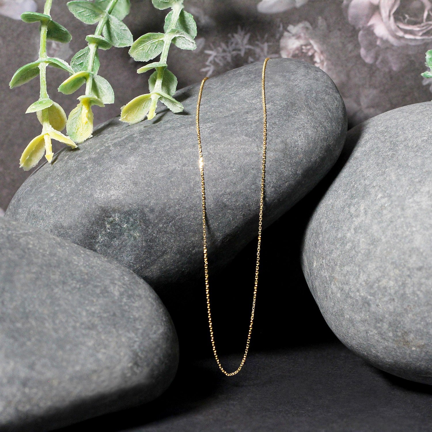 14k yellow gold diamond cut cable link chain draped over smooth gray stones.