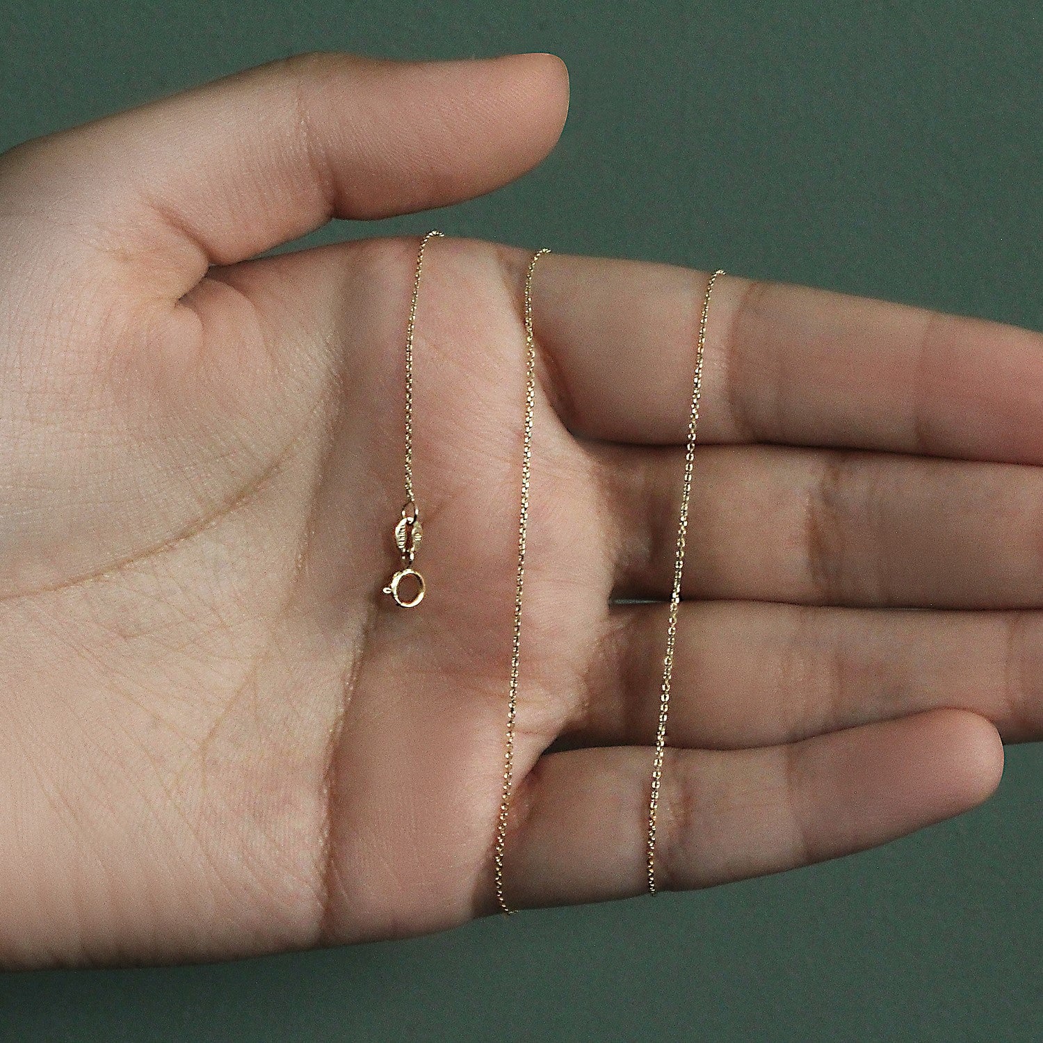 A delicate 14k yellow gold diamond cut cable link chain with a spring ring clasp is held in a hand.