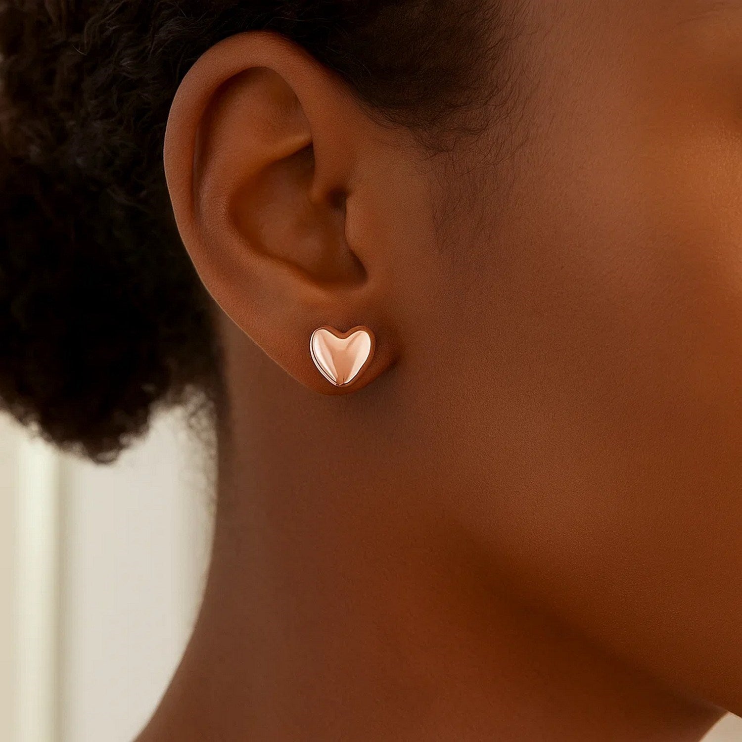 14k rose gold puffed heart shape shiny earrings on a person's ear.