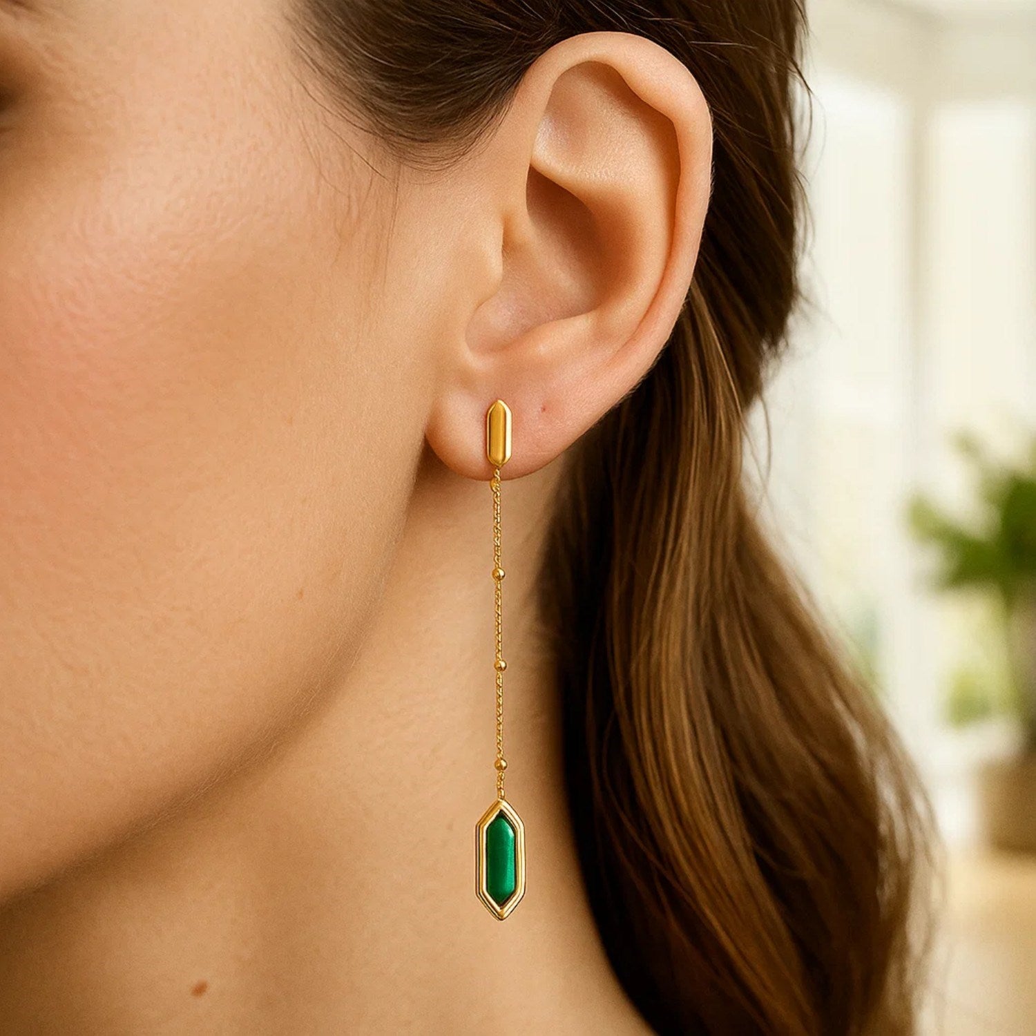 A woman wears a long 14K yellow gold earring with a hexagonal malachite drop.