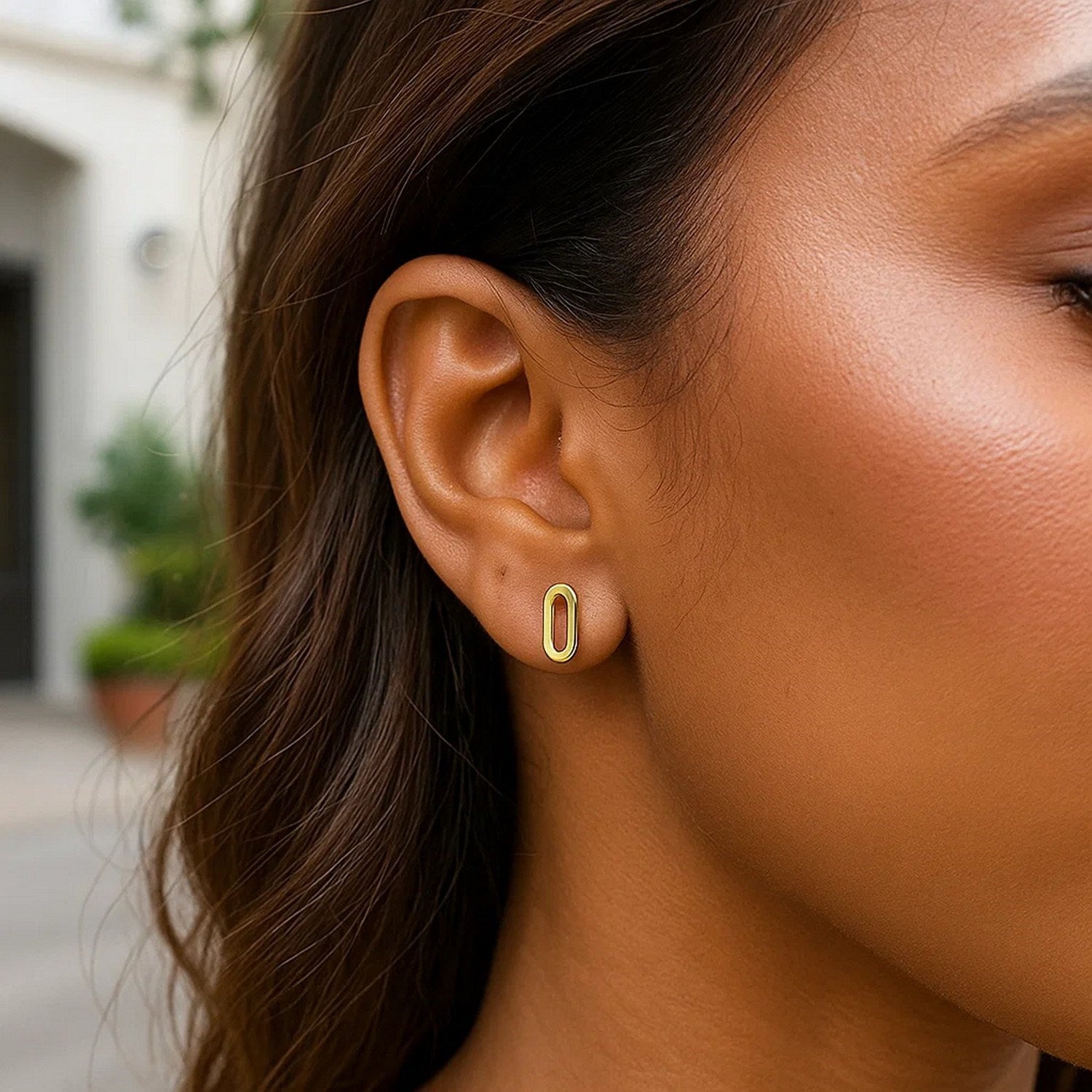 A woman wears a single 14k yellow gold paperclip link stud earring.