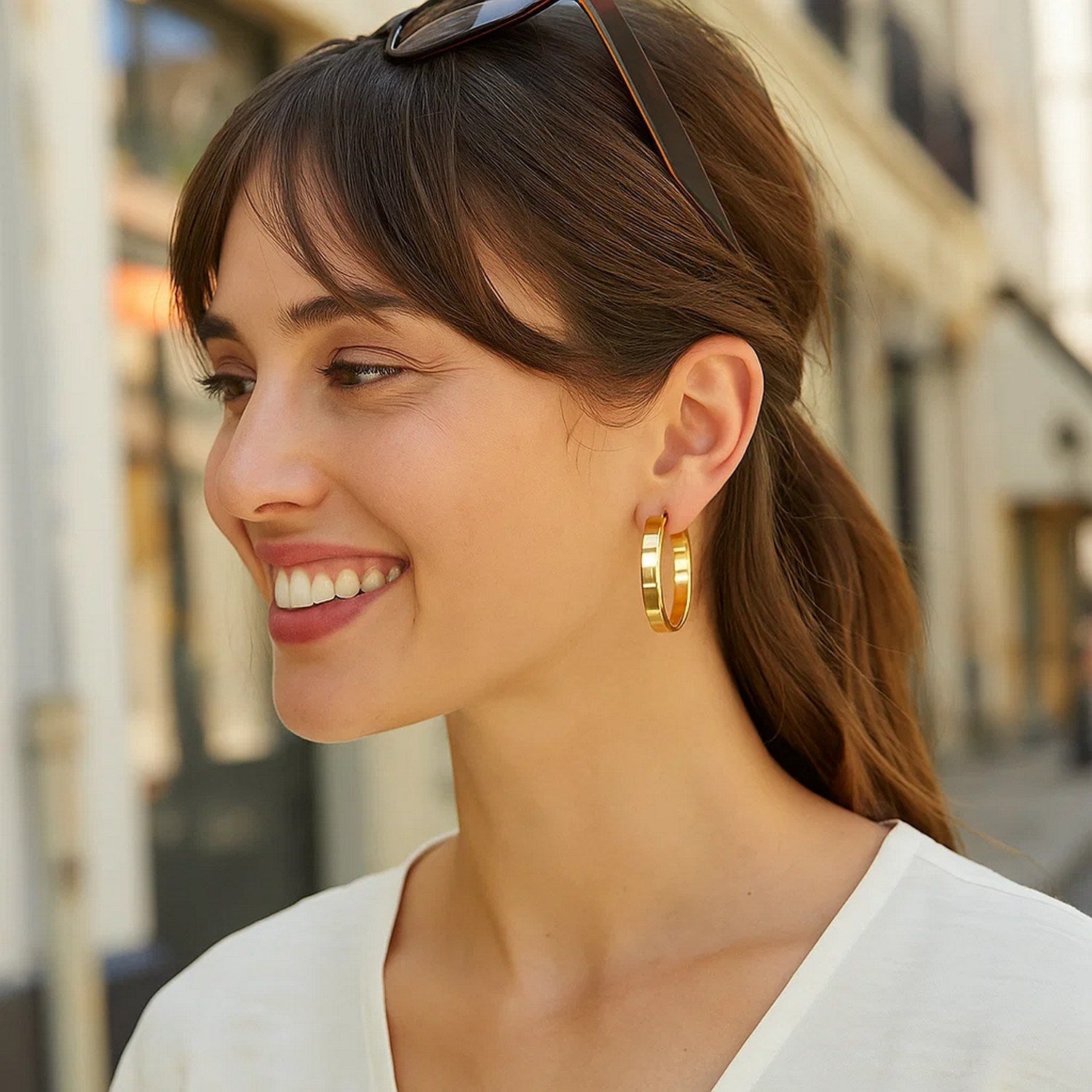 Large tube-shaped hoop earrings in 14K yellow gold on a smiling woman.