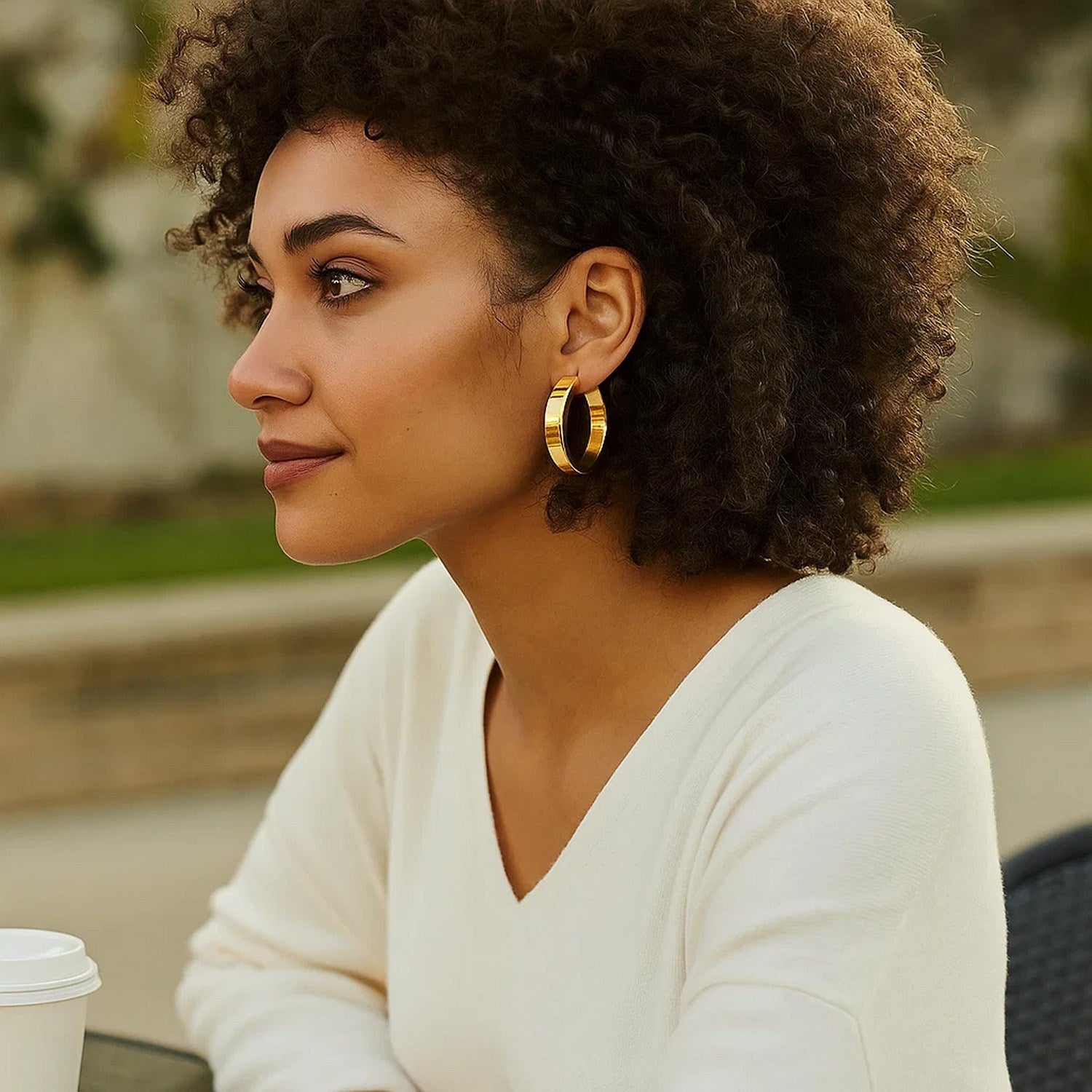 Large tube shaped hoop earrings in 14K yellow gold on a woman.