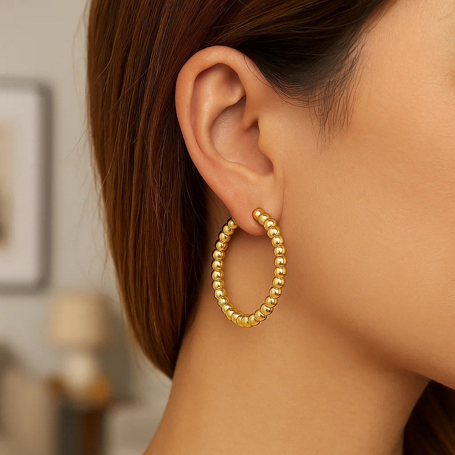 14K yellow gold polished large bead hoop earrings are worn on a woman's ear.