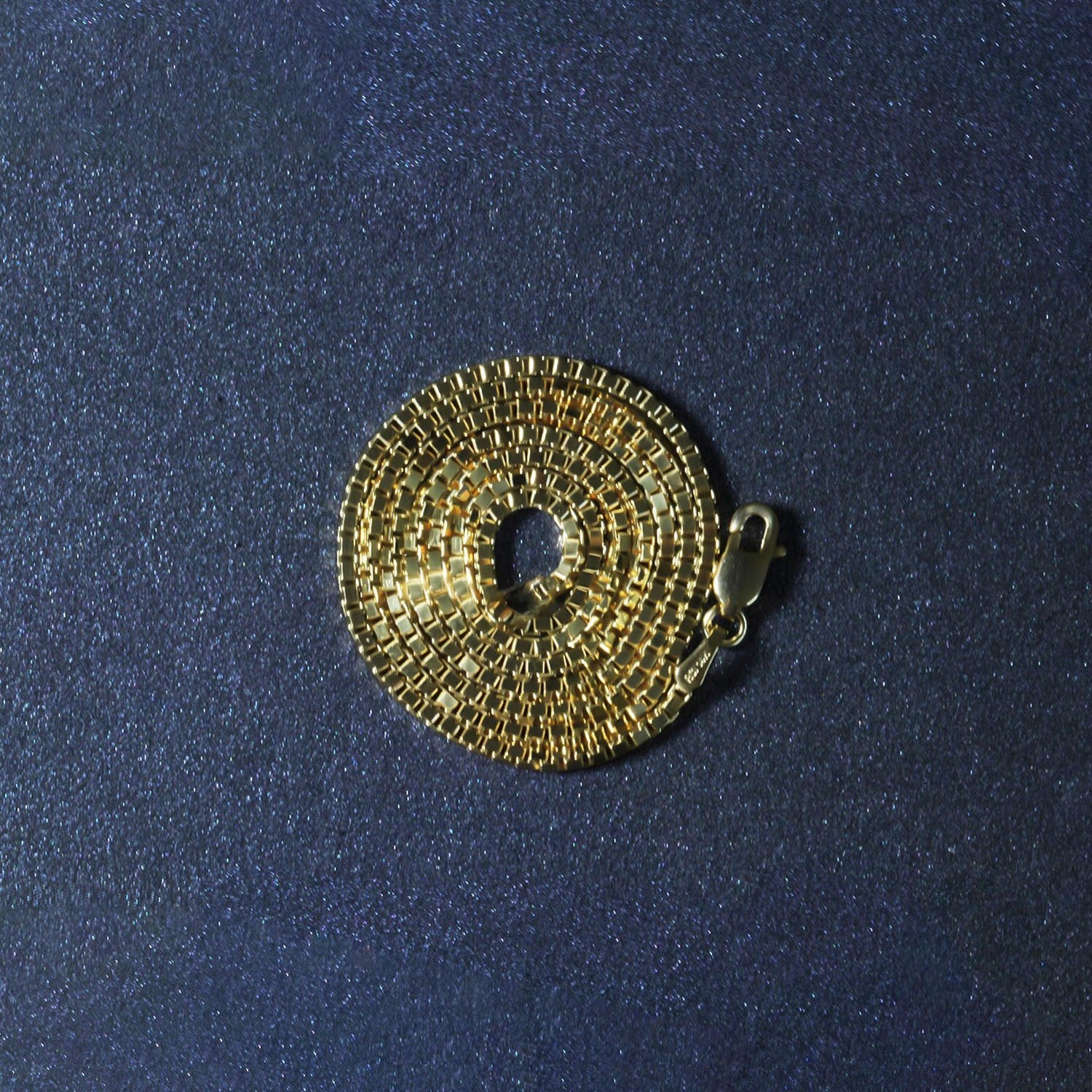 14K yellow gold classic box chain with a lobster clasp, coiled on a dark background.