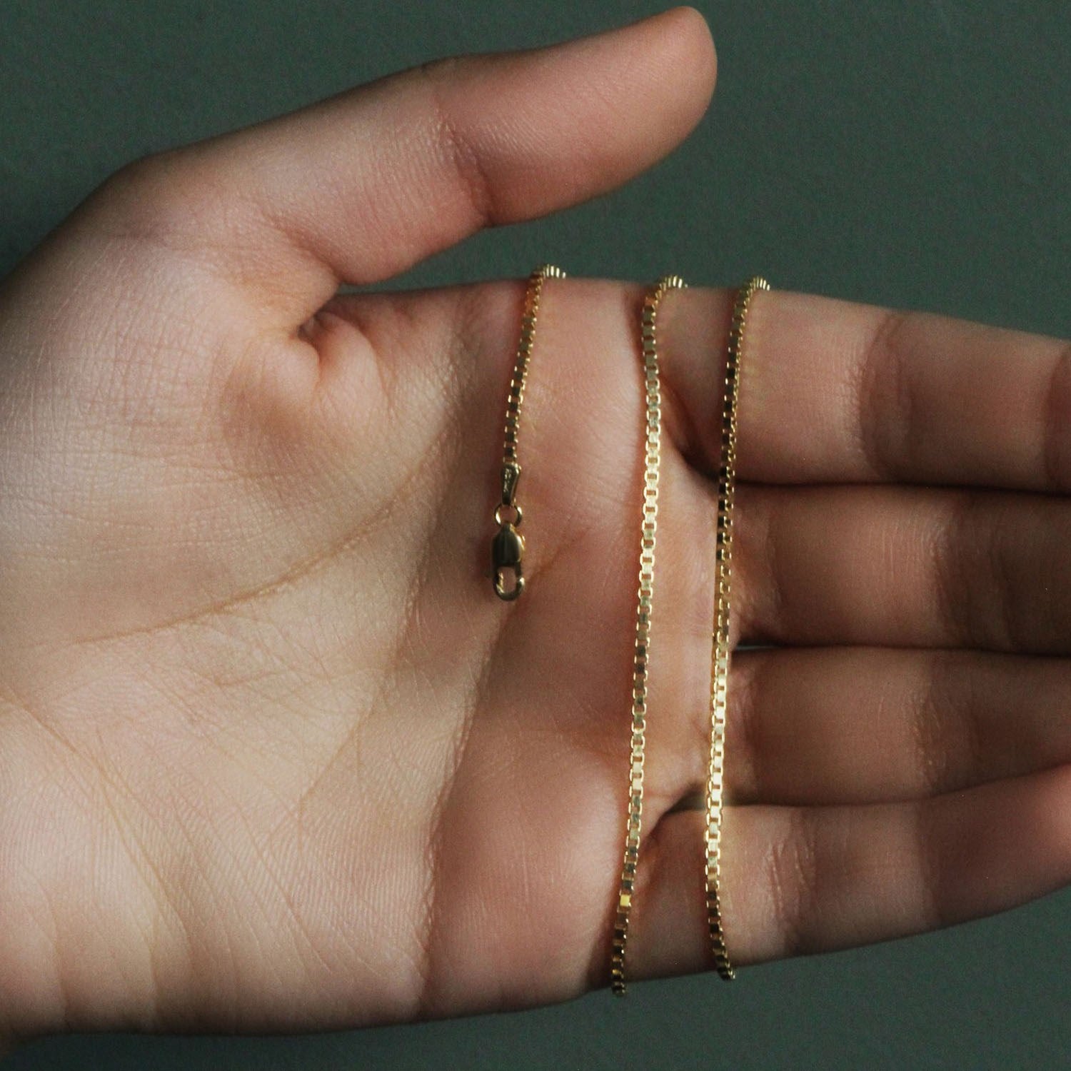 14K yellow gold classic box chain with a lobster clasp held in a hand.