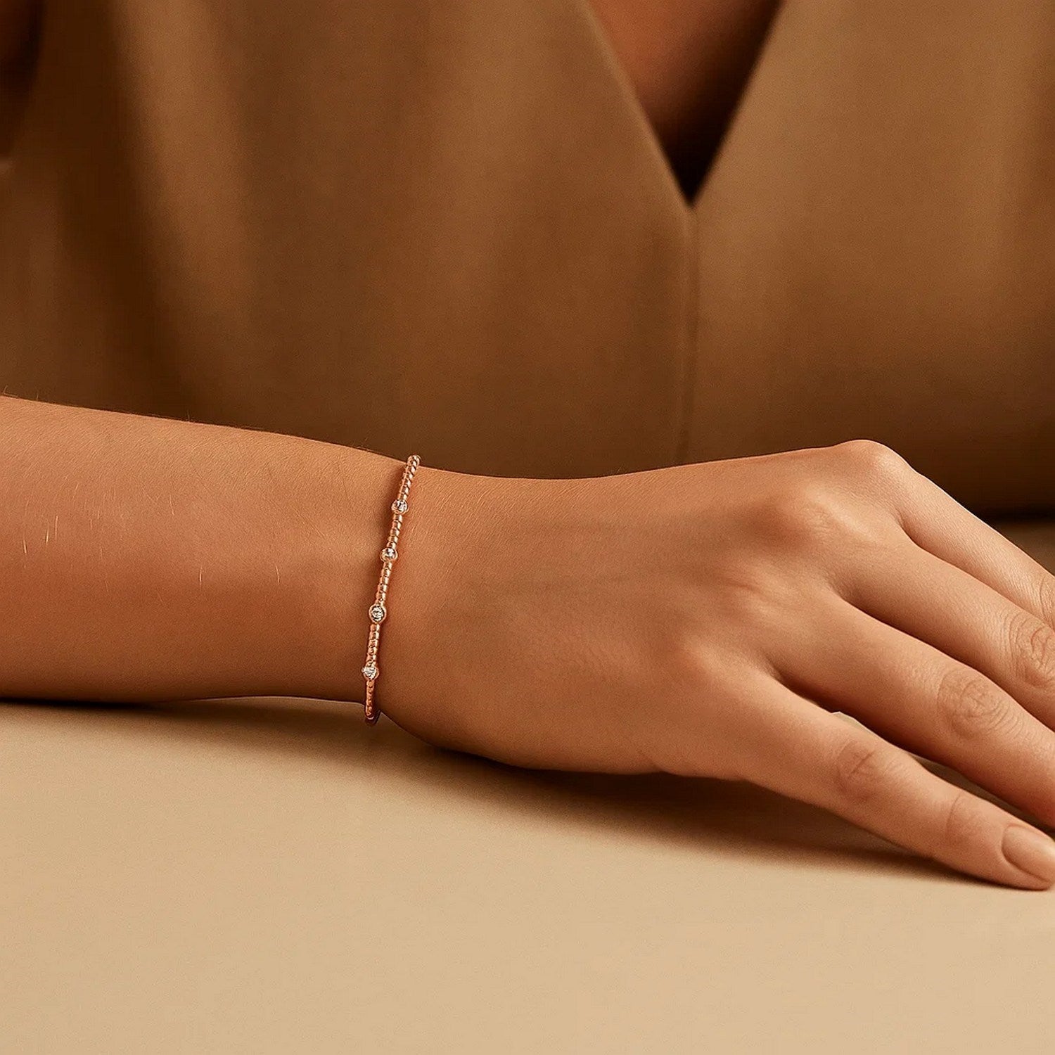 A 14K rose gold beaded bracelet with three small diamonds on a woman's wrist.