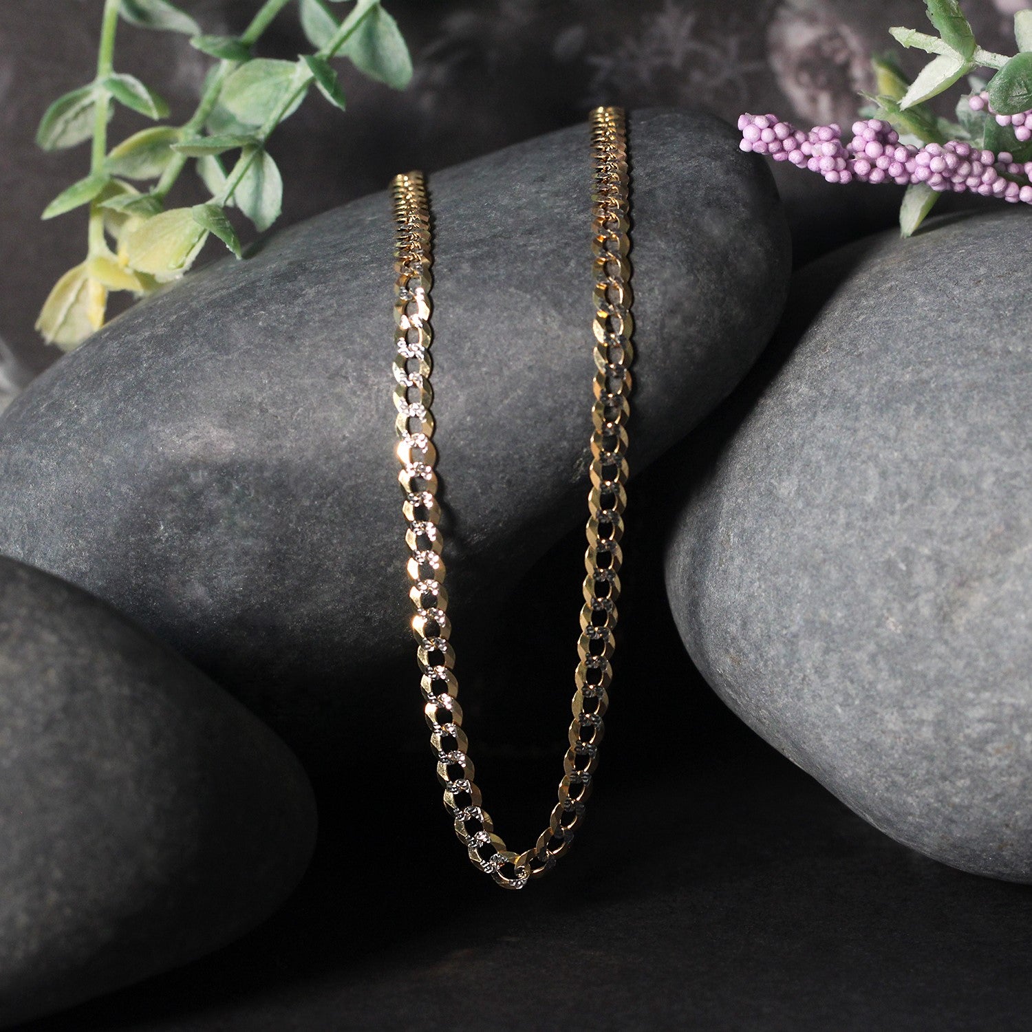 A 14k two-tone gold pave curb chain rests on dark gray stones.