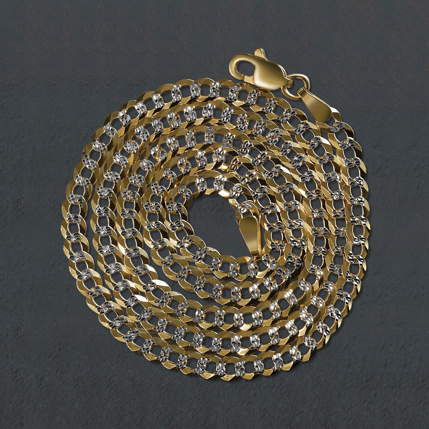 14k two-tone gold pave curb chain with a lobster clasp, coiled on a dark surface.