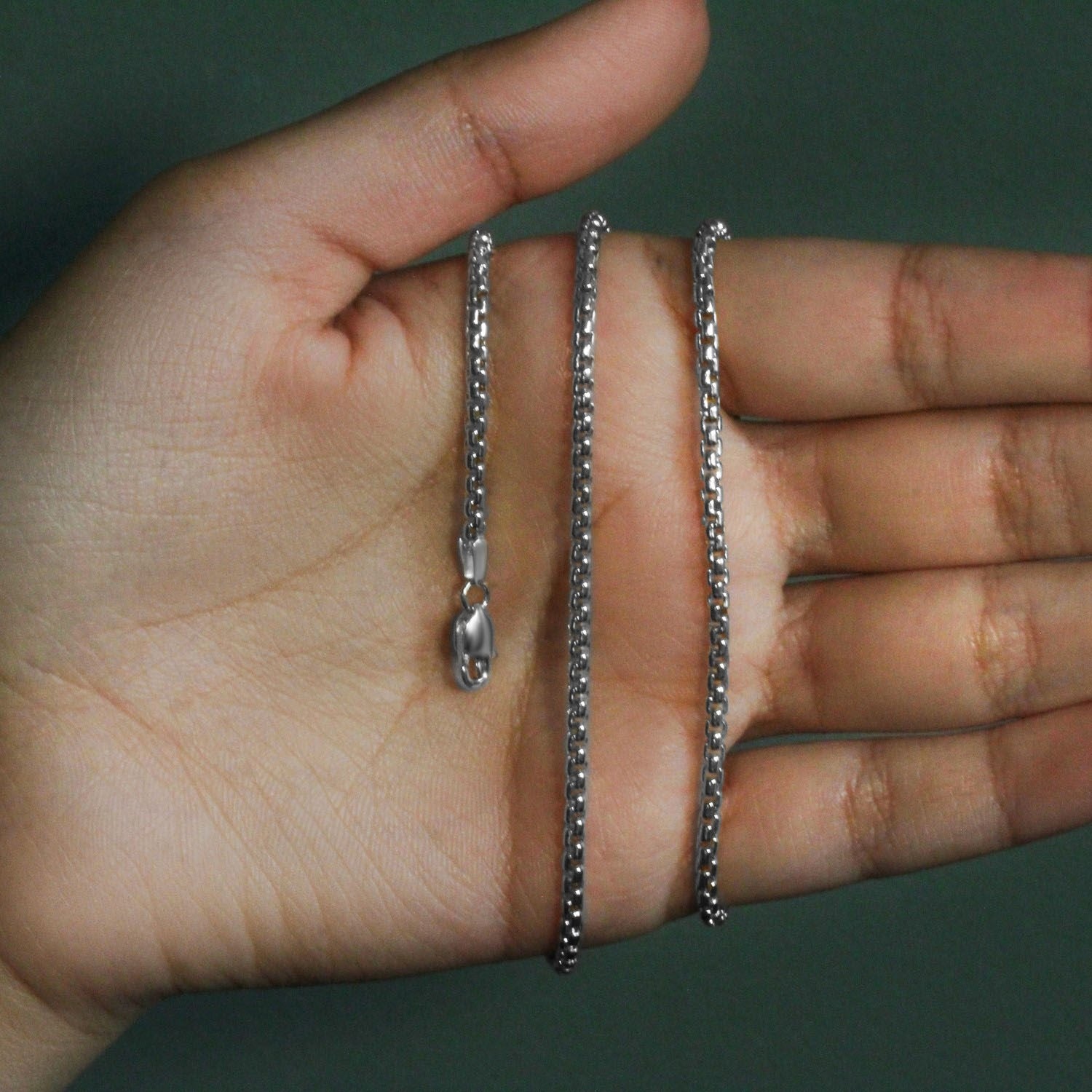 14k white gold solid round box chain with a lobster clasp held in a hand.