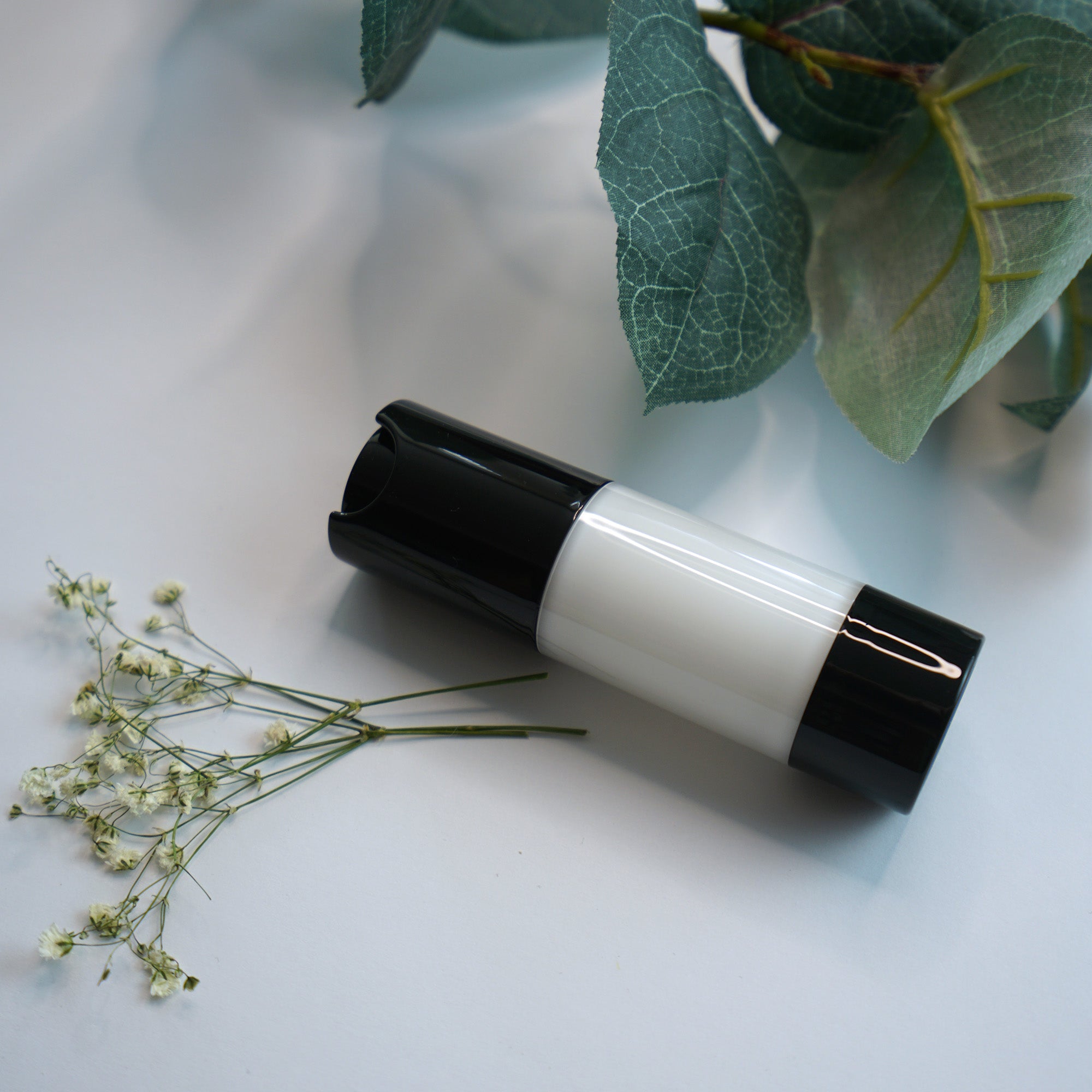 A black and white bottle of Extreme Moisture Blend lies on a white surface with flowers and leaves.