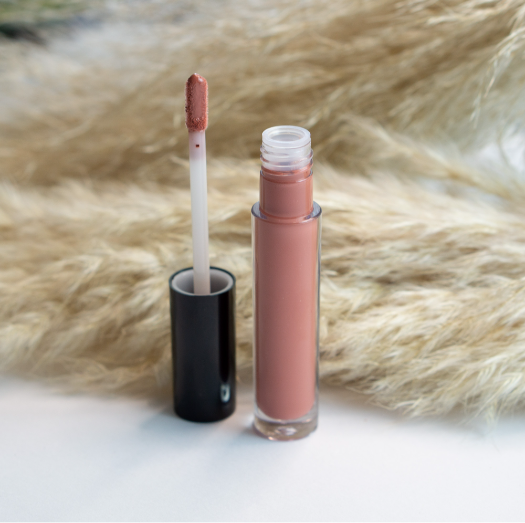 An open tube of nude lip gloss with its applicator wand on a textured background.
