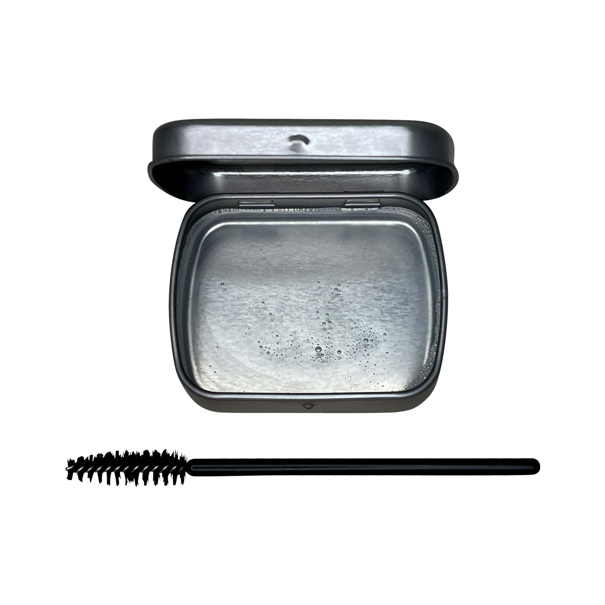 An open tin of clear brow soap with a black spoolie brush.