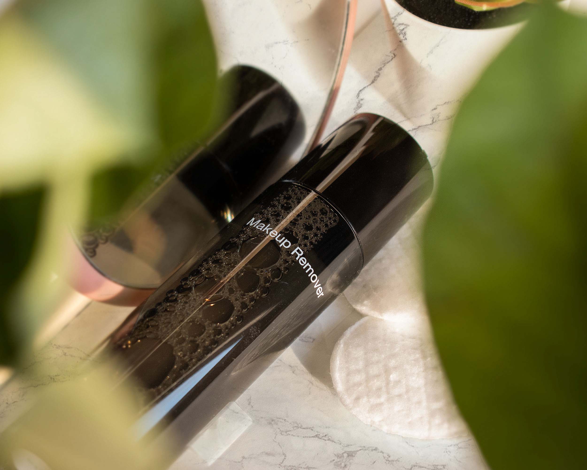 A black bottle of makeup remover with bubbles is shown on a marble surface.