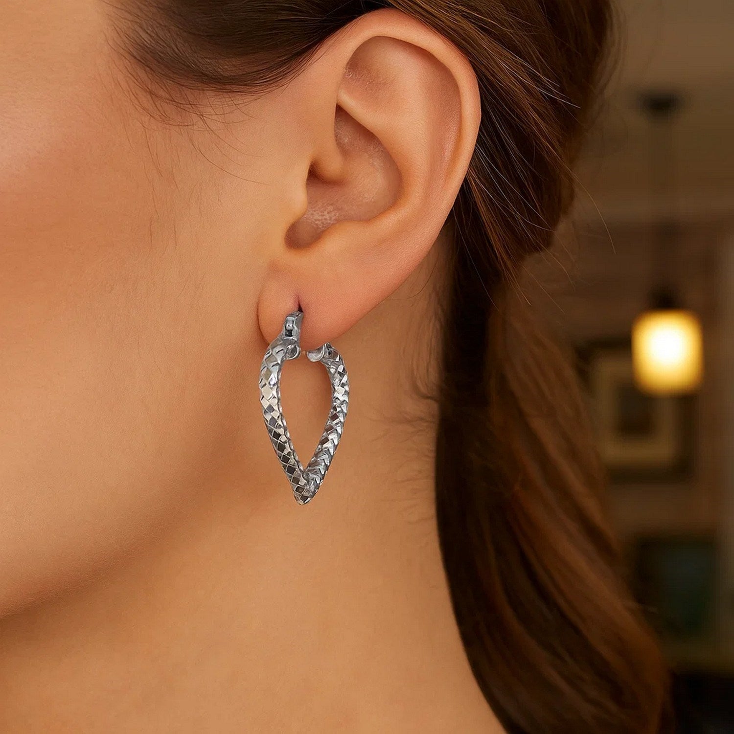 Sterling silver rhodium plated heart-style hoop diamond cut earrings on a woman's ear.