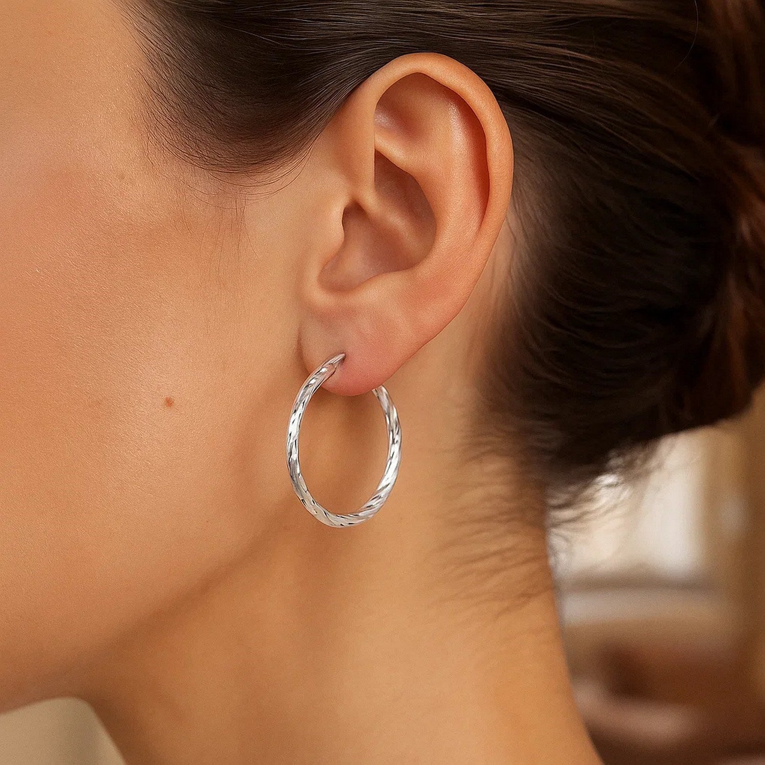 Sterling silver diamond-cut hoop earrings with rhodium plating on a model.
