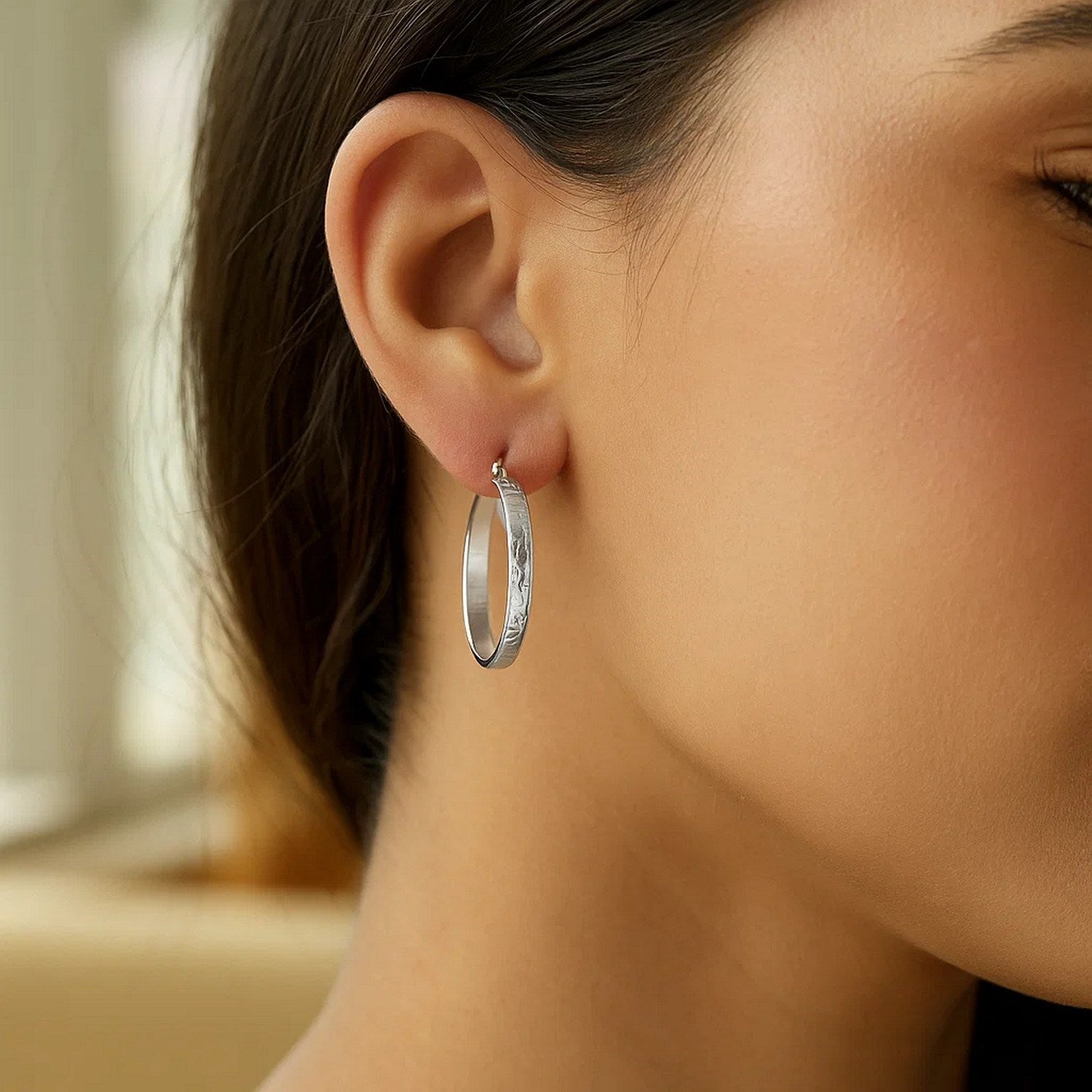 Sterling silver hammered hoop earrings with rhodium plating on a model's ear.