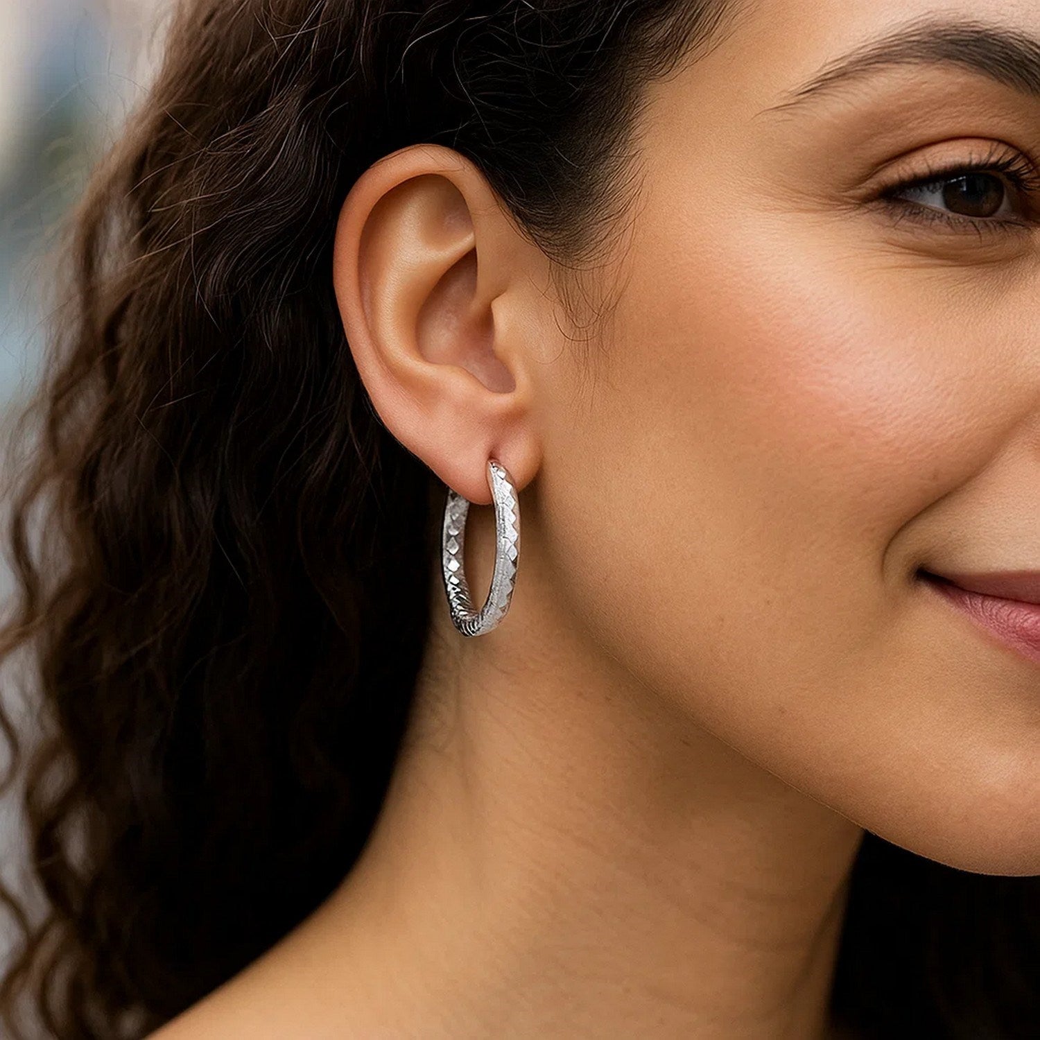 Sterling silver faceted motif large hoop earrings with rhodium plating on a model.