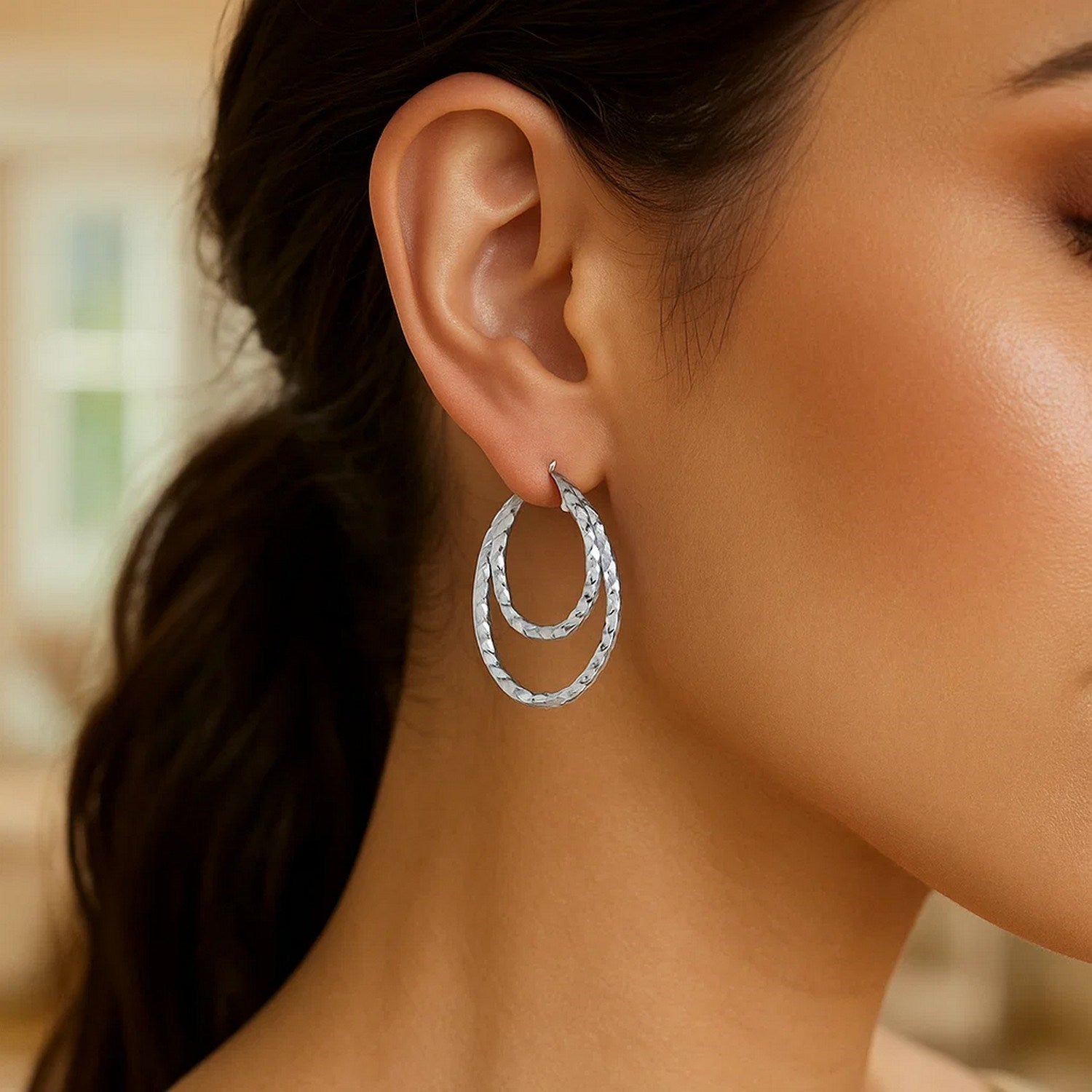 Sterling silver double oval textured hoop earrings on a woman's ear.