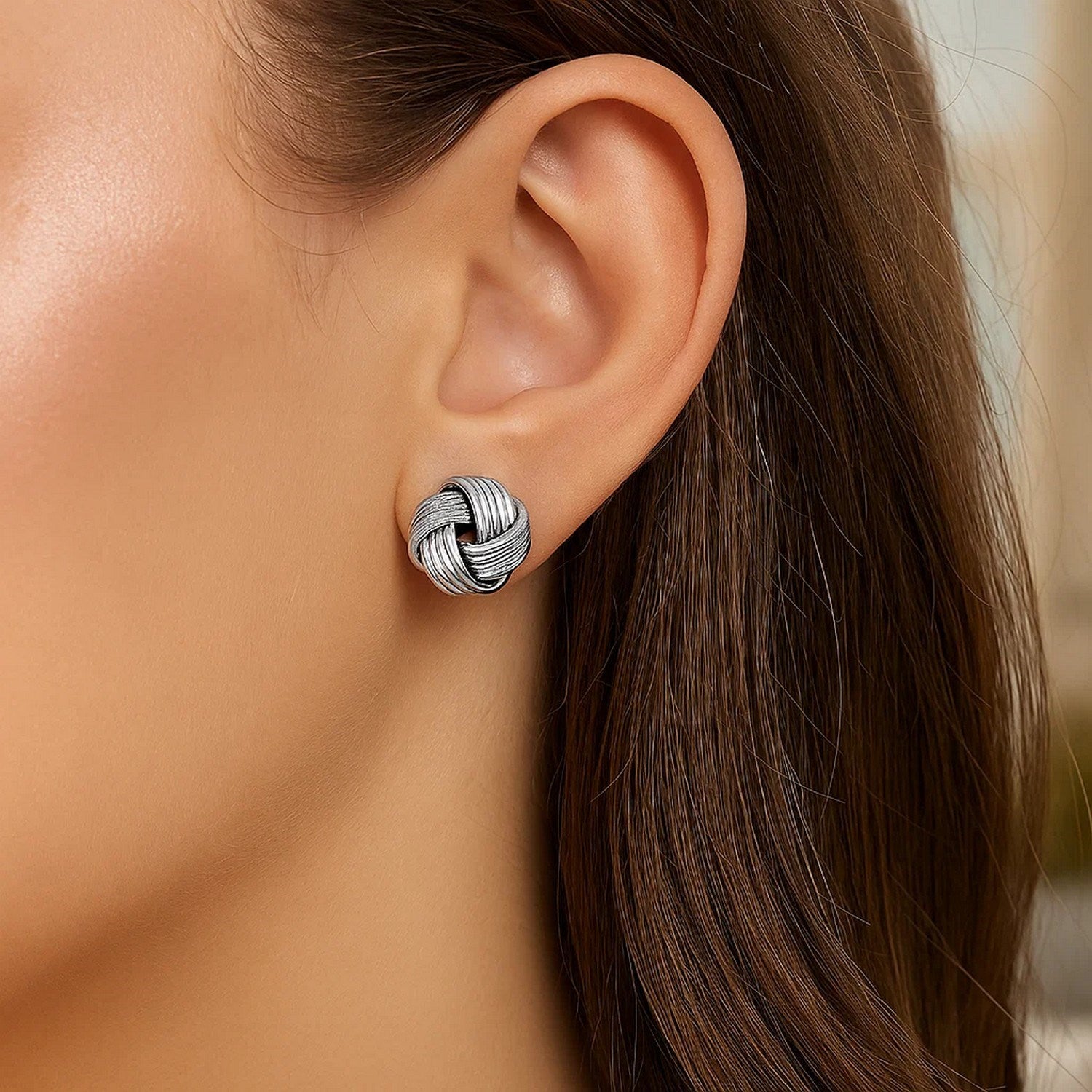 Sterling silver groove textured love knot earrings on a person's ear.