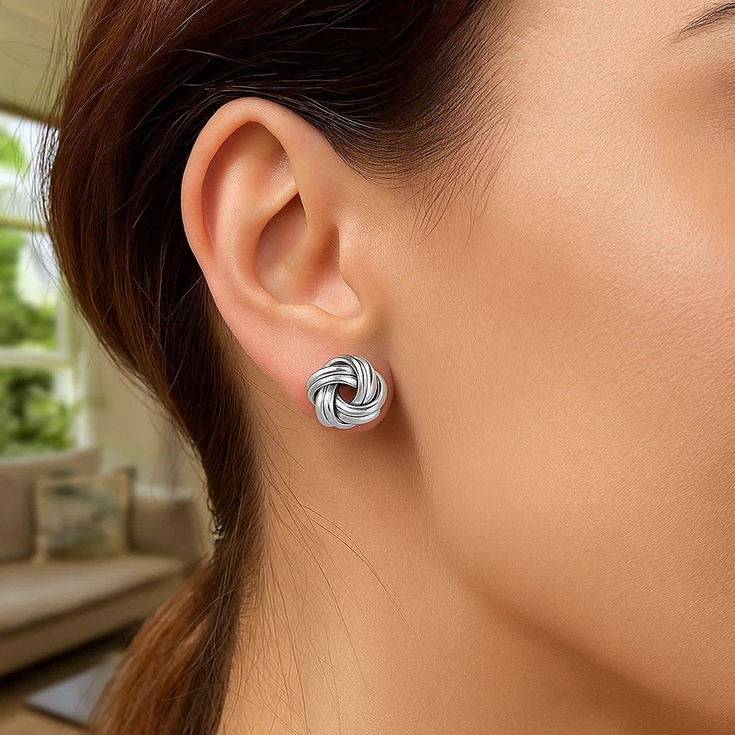 Sterling silver polished two-strand love knot earrings on a woman's ear.