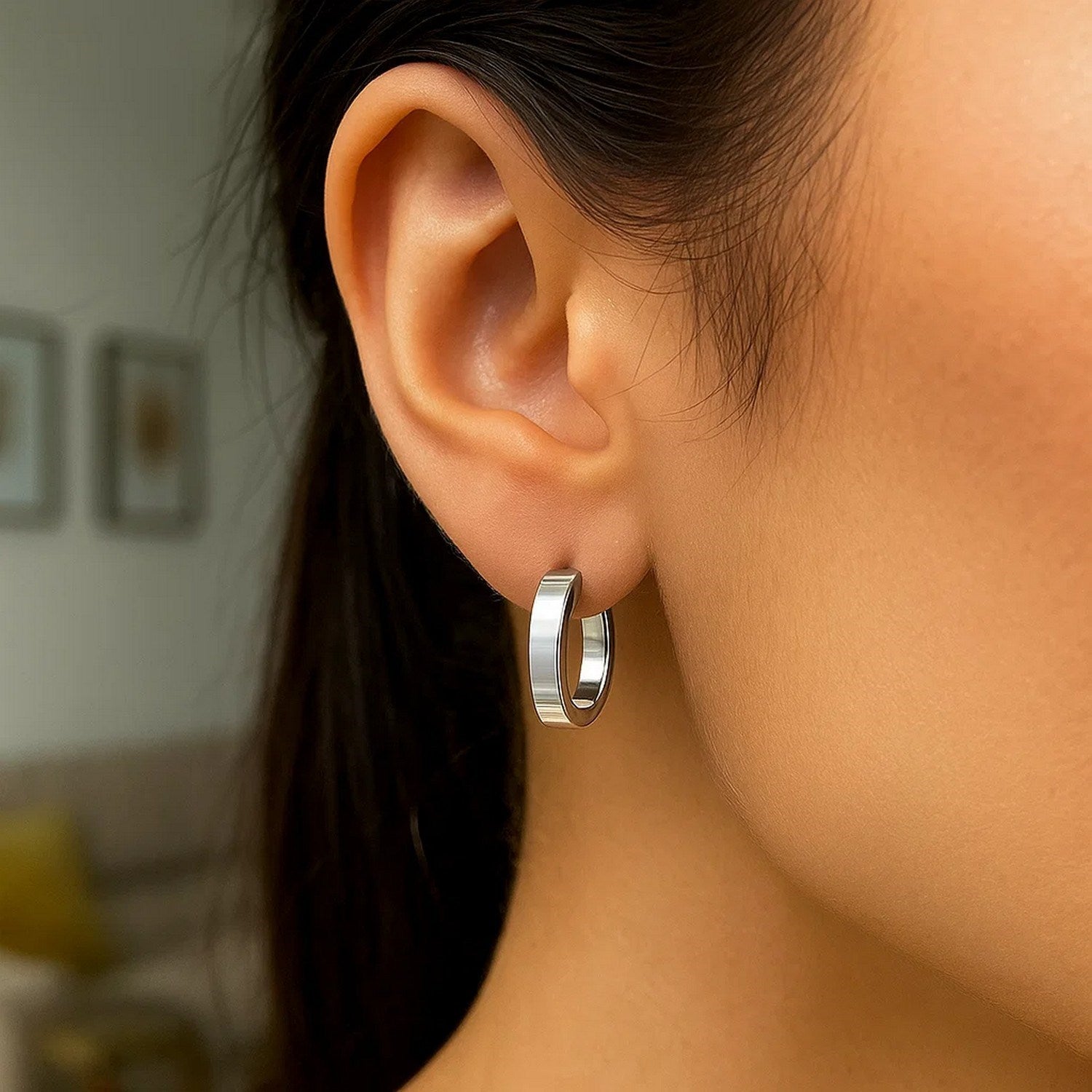 Sterling silver flat style oval hoop earrings with rhodium plating on a person's ear.
