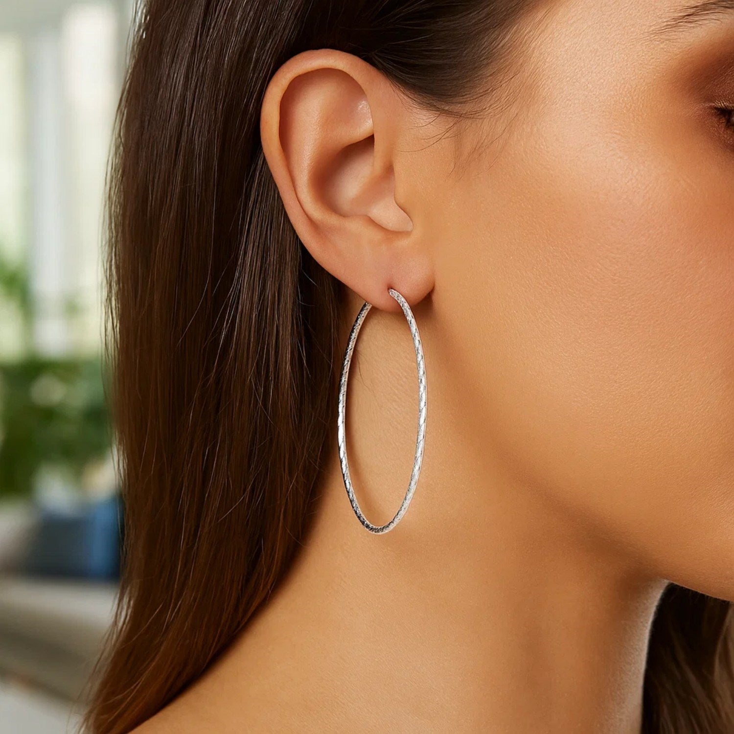 A woman wears large, textured sterling silver hoop earrings.