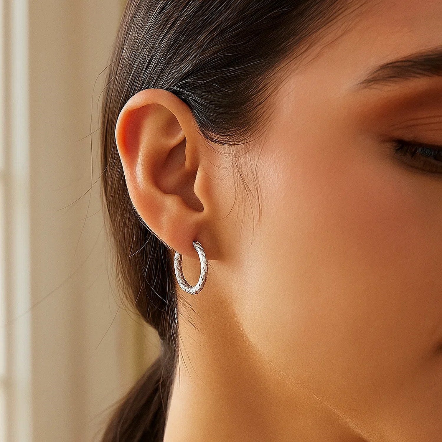 Sterling silver faceted hoop earrings with rhodium plating on a woman's ear.