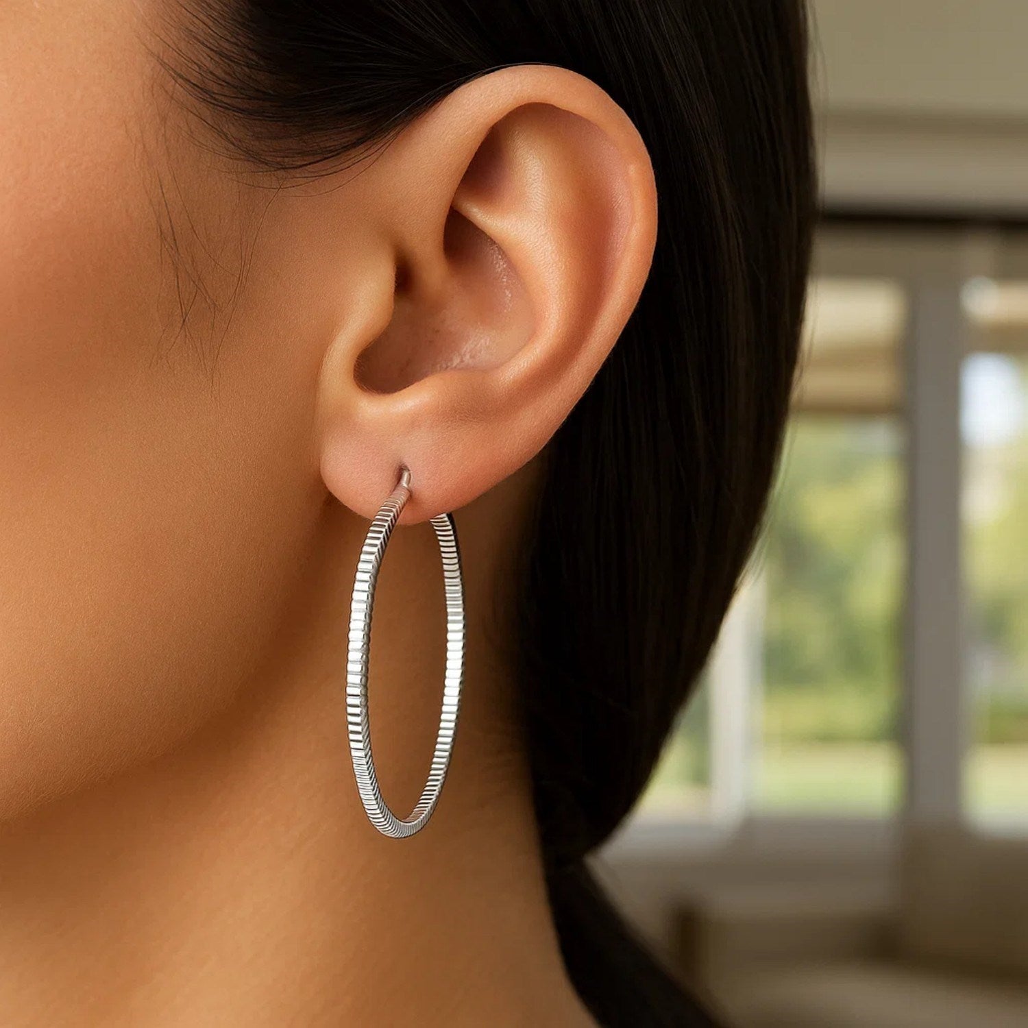 A woman wears a single sterling silver ridge textured hoop earring.
