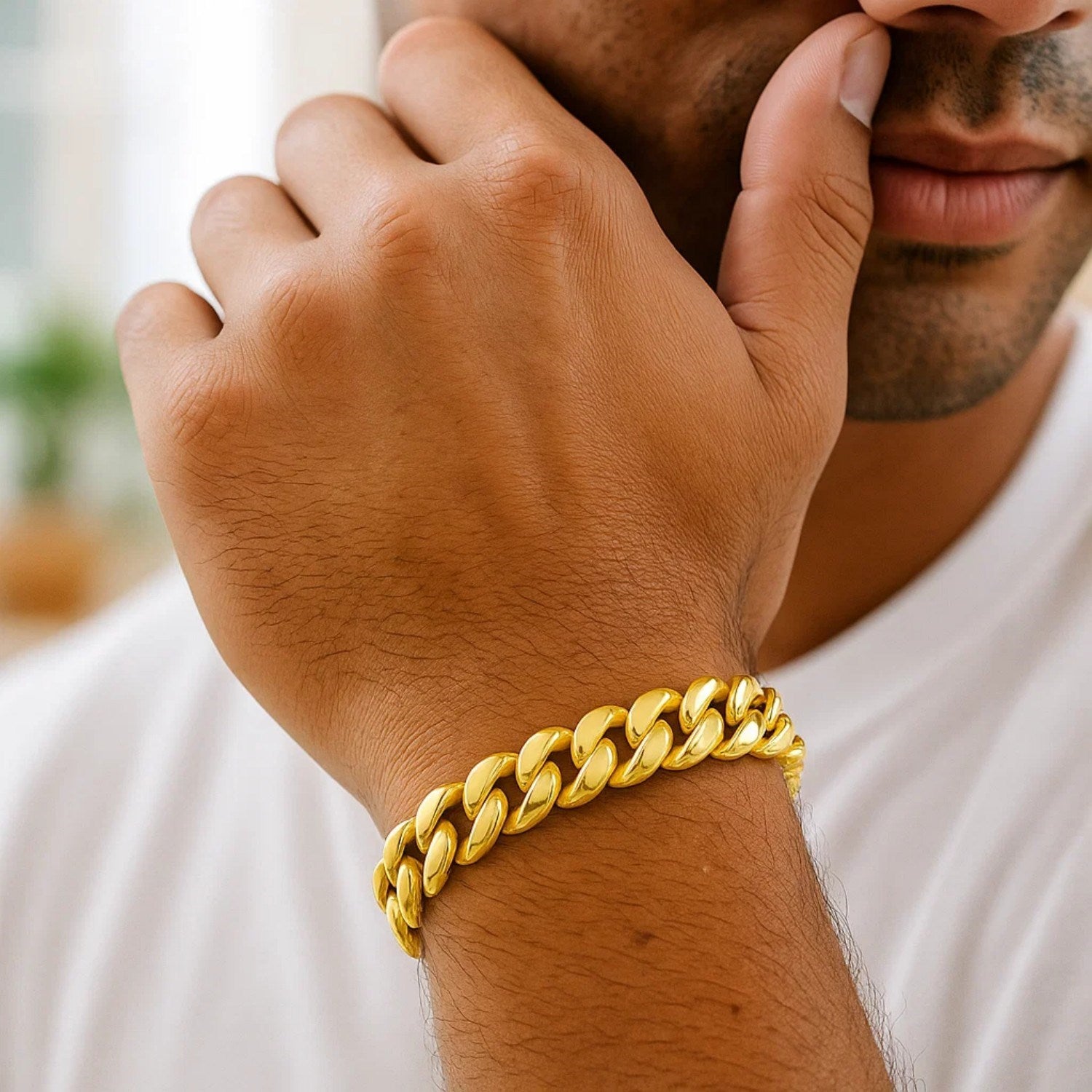 A man wears a thick, shiny 14k yellow gold Miami Cuban bracelet on his left wrist.