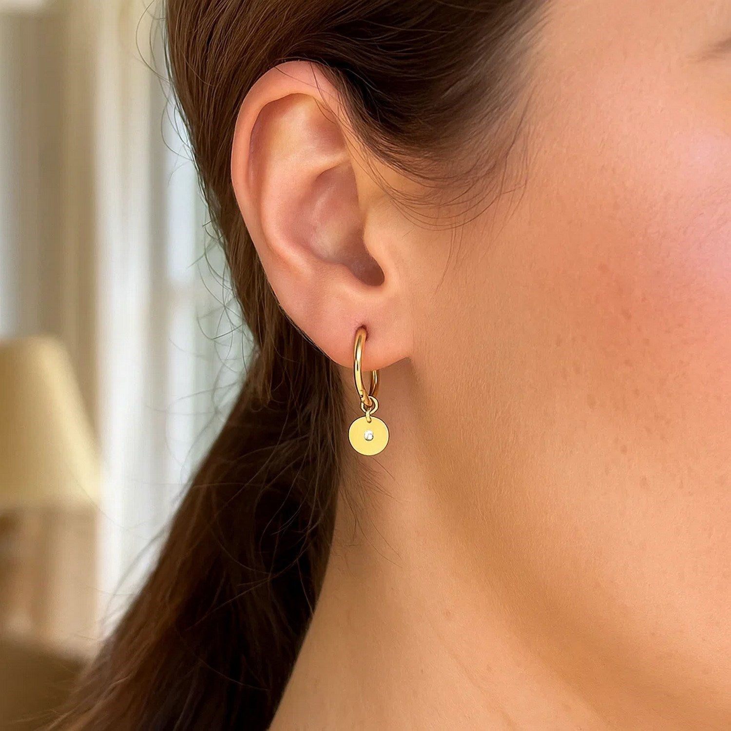 14K yellow gold hoop earrings with diamond disc charms on a woman's ear.