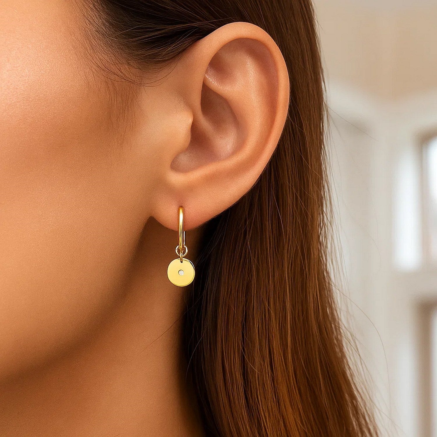 14K yellow gold hoop earrings with a diamond disc charm on a woman's ear.