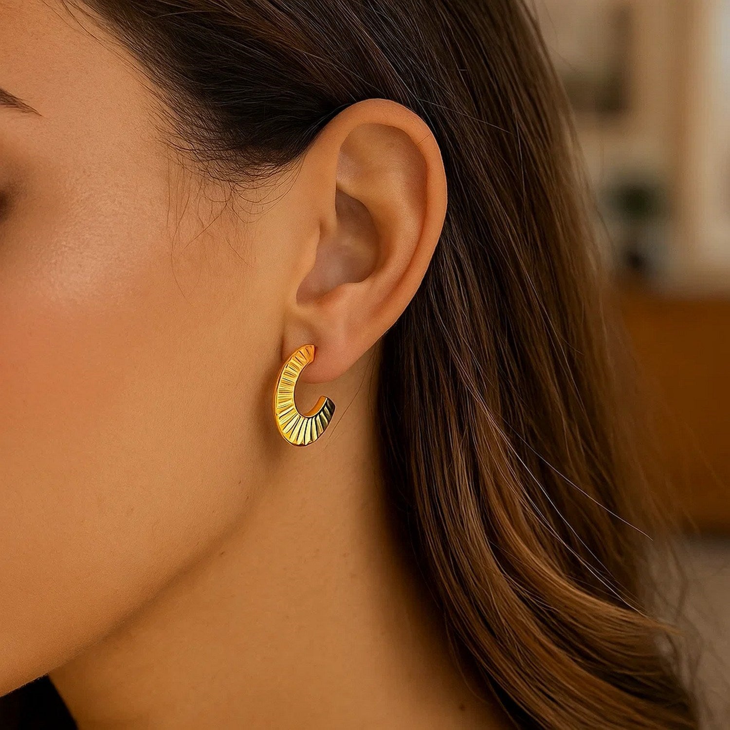 A woman wears a single 14K yellow gold graduated scalloped pointed half hoop earring.