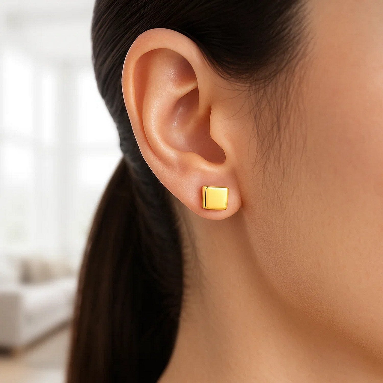 14k yellow gold polished cube post earrings are worn on a person's ear.