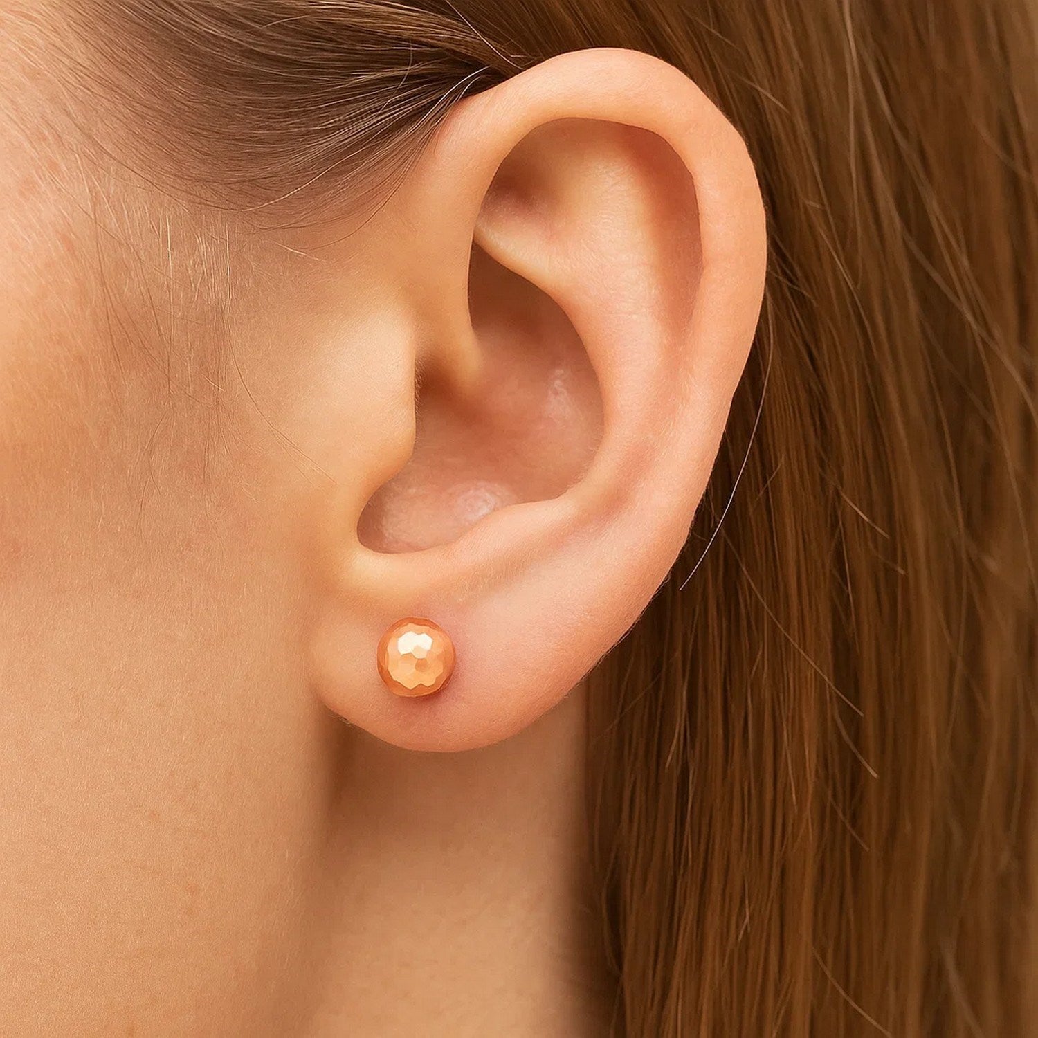 A single 14k rose gold faceted ball earring is worn on an ear.