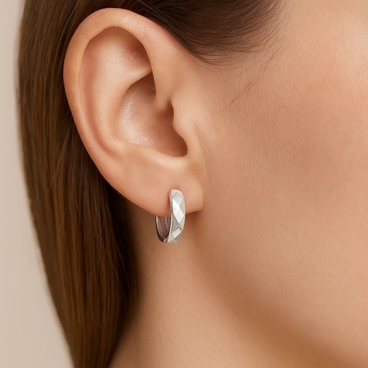 A woman wears a single 14K white gold faceted huggie earring.