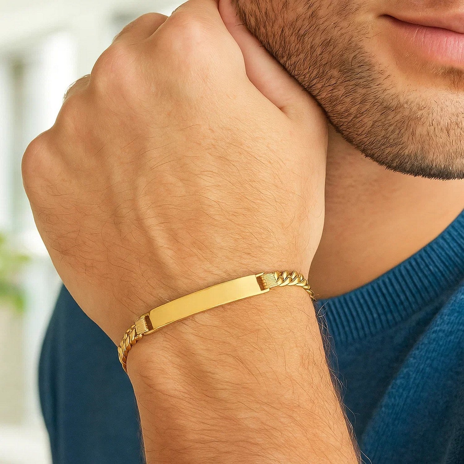 A man wears a 14K yellow gold Cuban ID bracelet on his left wrist.
