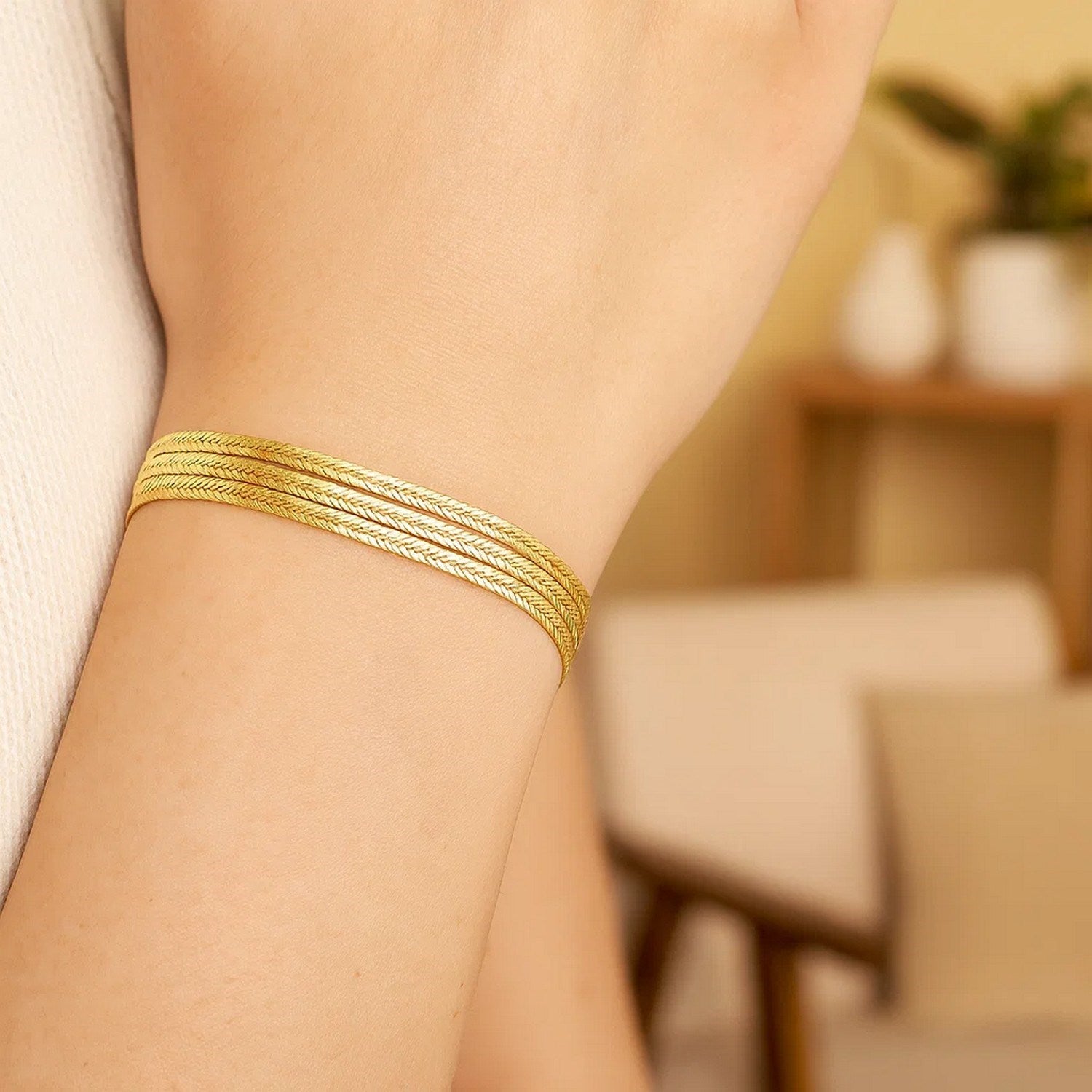 A 14k yellow gold three-strand herringbone chain bracelet on a person's wrist.