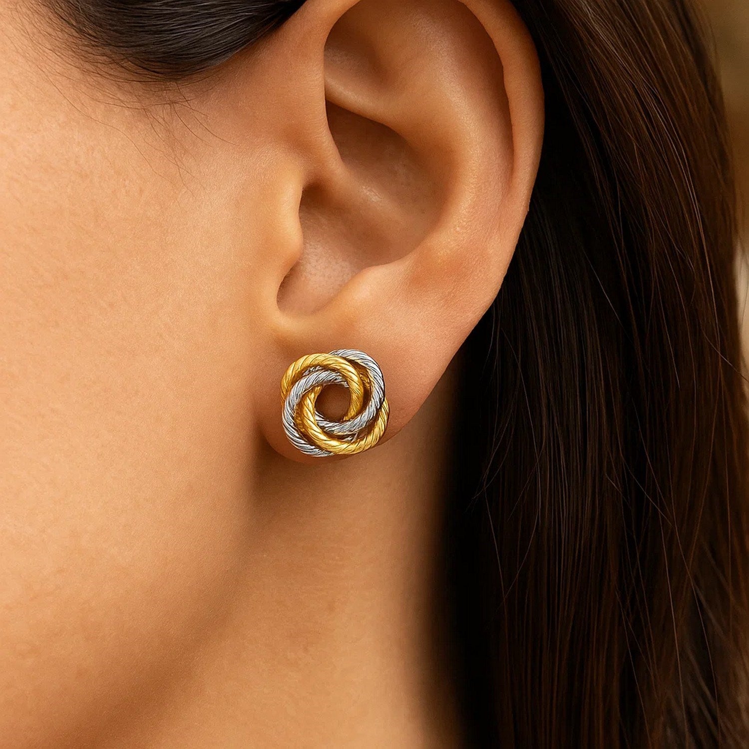 14k two-tone gold love knot earrings on a woman's ear.