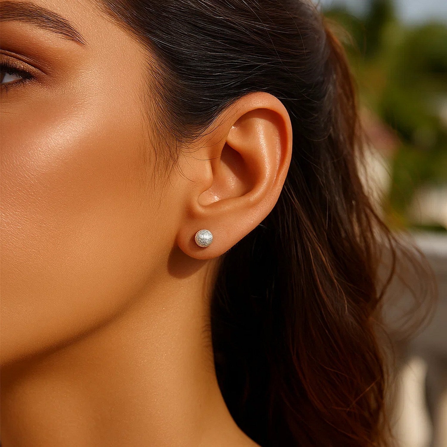 14k white gold ball earrings with a crystal cut texture on a woman's ear.