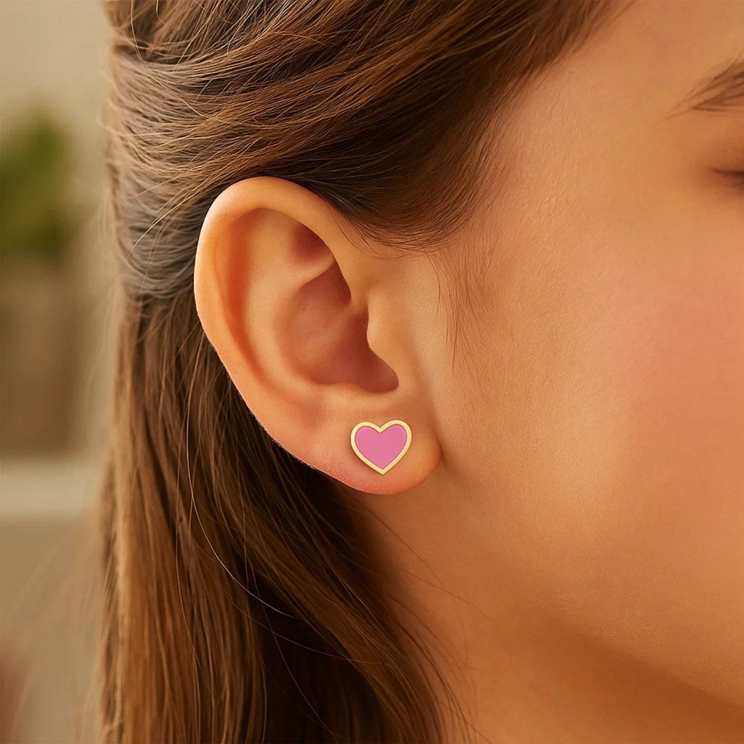 14k yellow gold and enamel pink heart stud earrings on a person's ear.