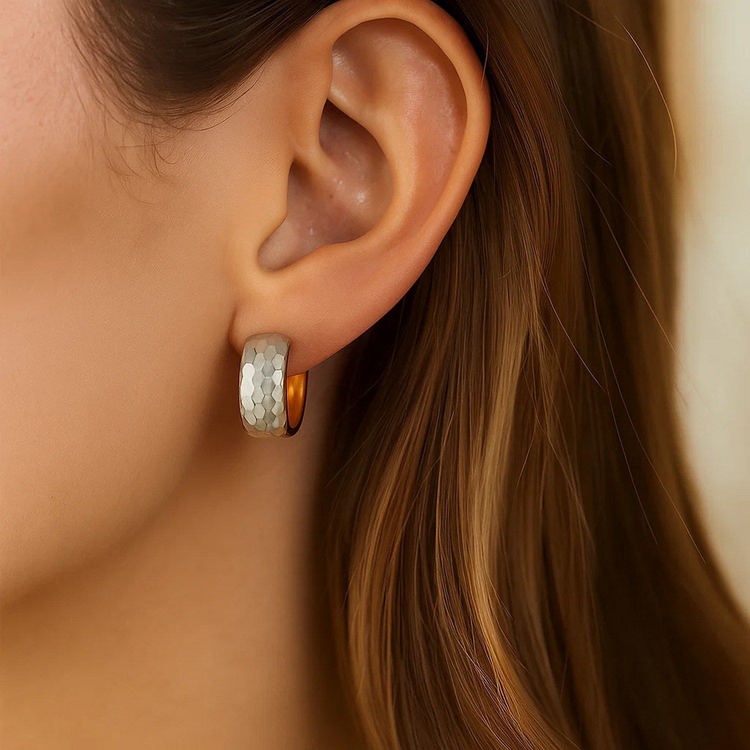 A woman wears a two-tone gold, diamond-cut hoop earring.