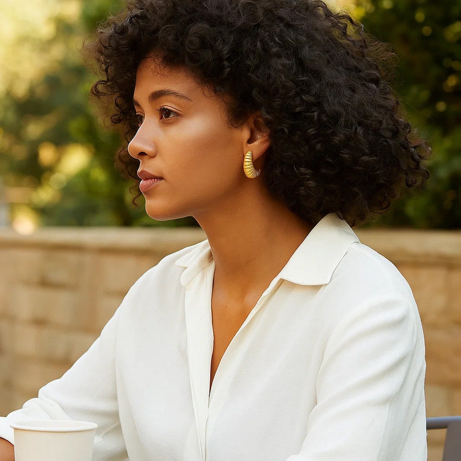 Puffy graduated ribbed shell hoop earrings in 14K yellow gold on a woman.