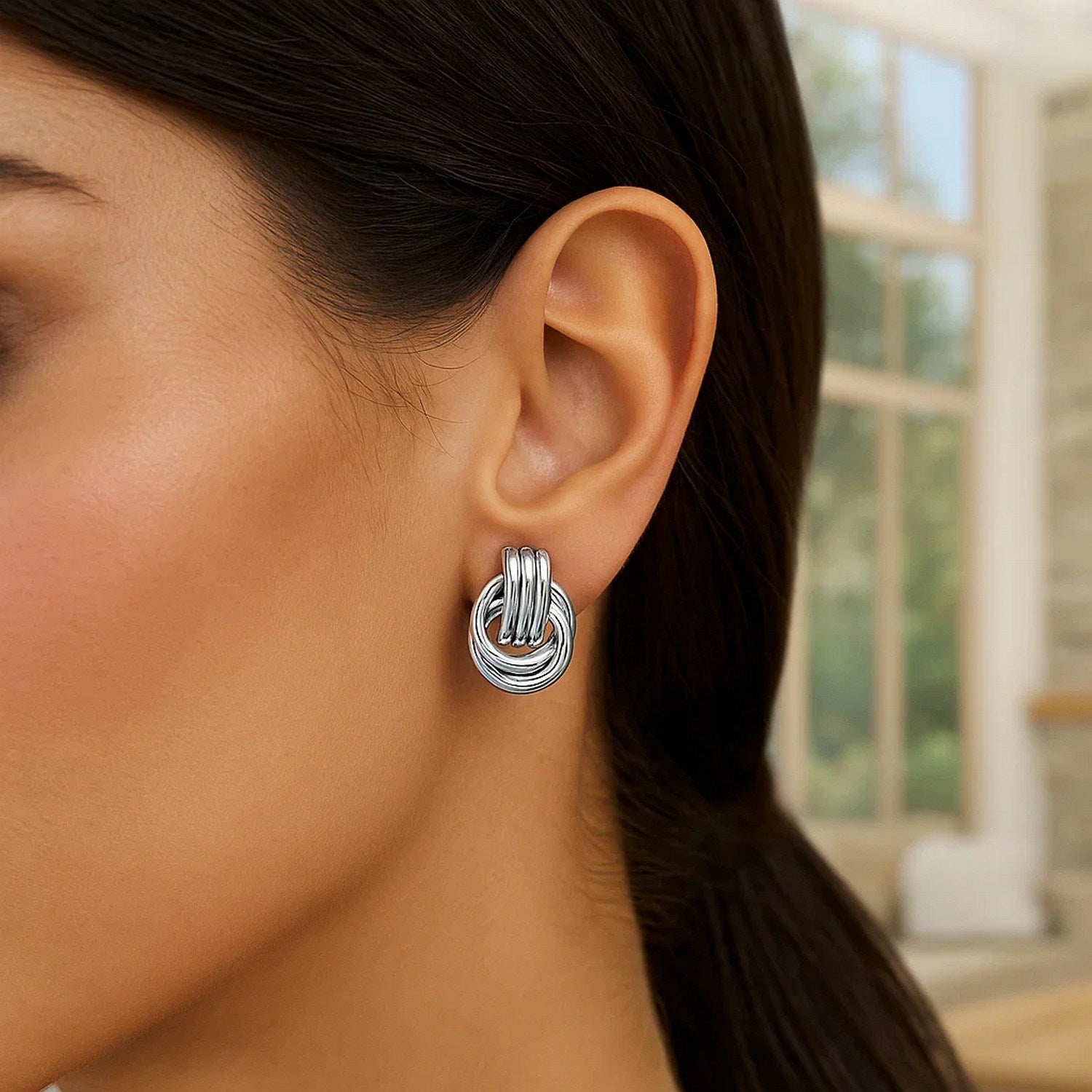 Polished sterling silver love knot earrings with interlocking rings on a woman's ear.
