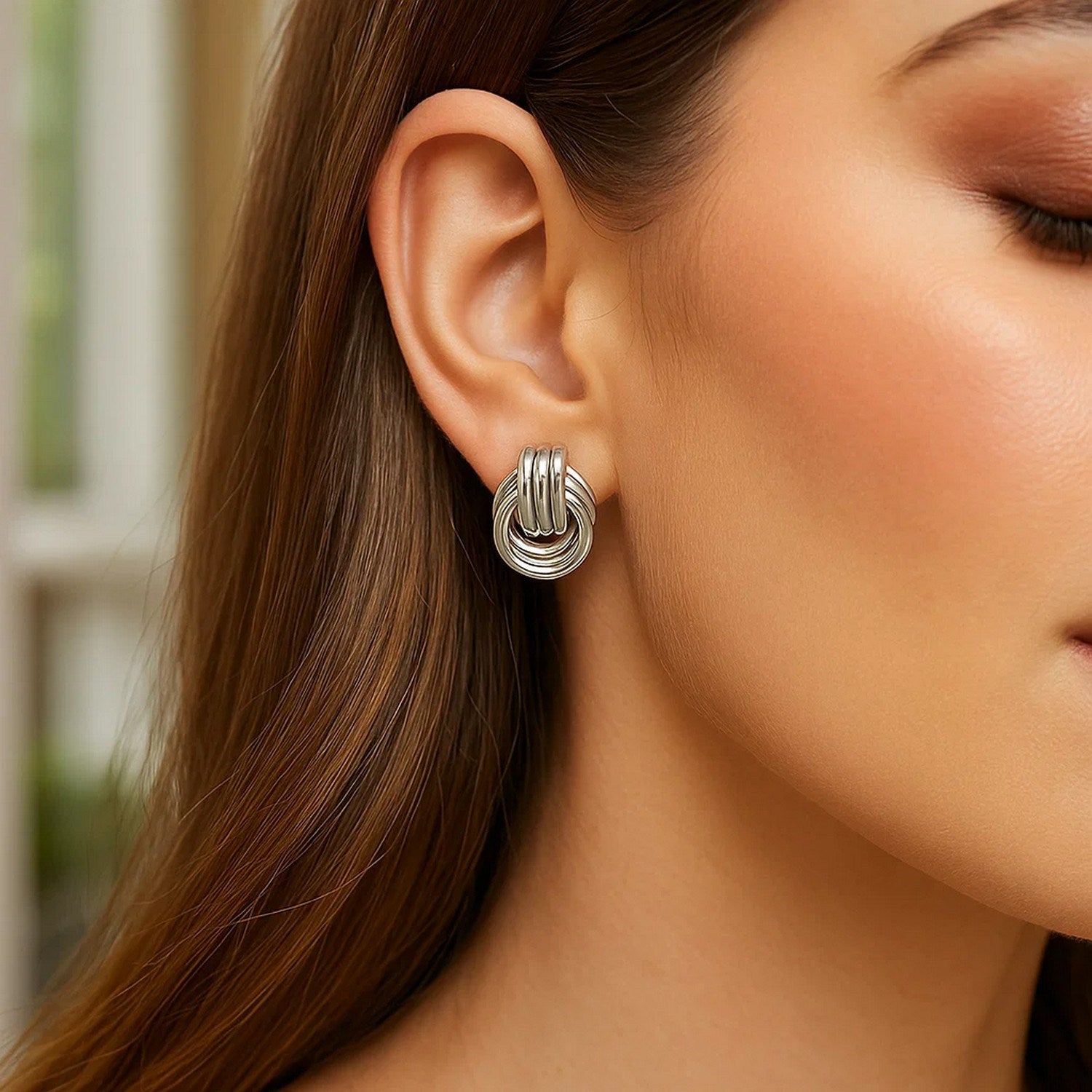 Polished sterling silver love knot earrings with interlocking rings on a woman's ear.