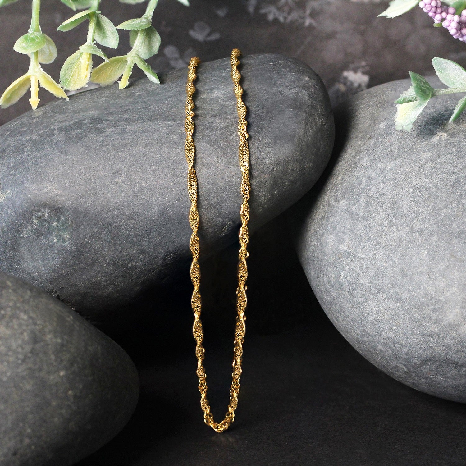 14k yellow gold Singapore chain with a lobster clasp, displayed on dark grey rocks.