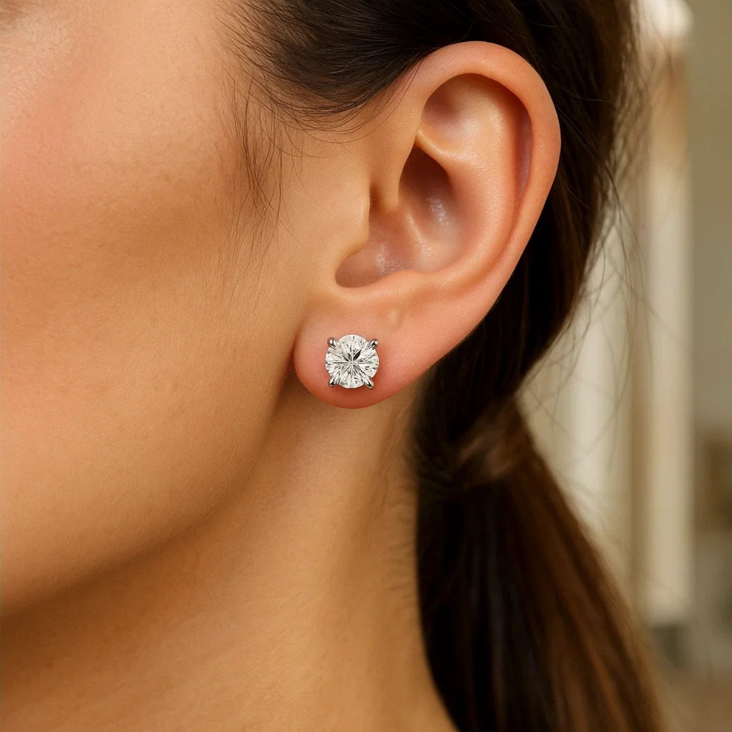 Sterling silver round CZ stud earrings with a four-prong setting on an ear.