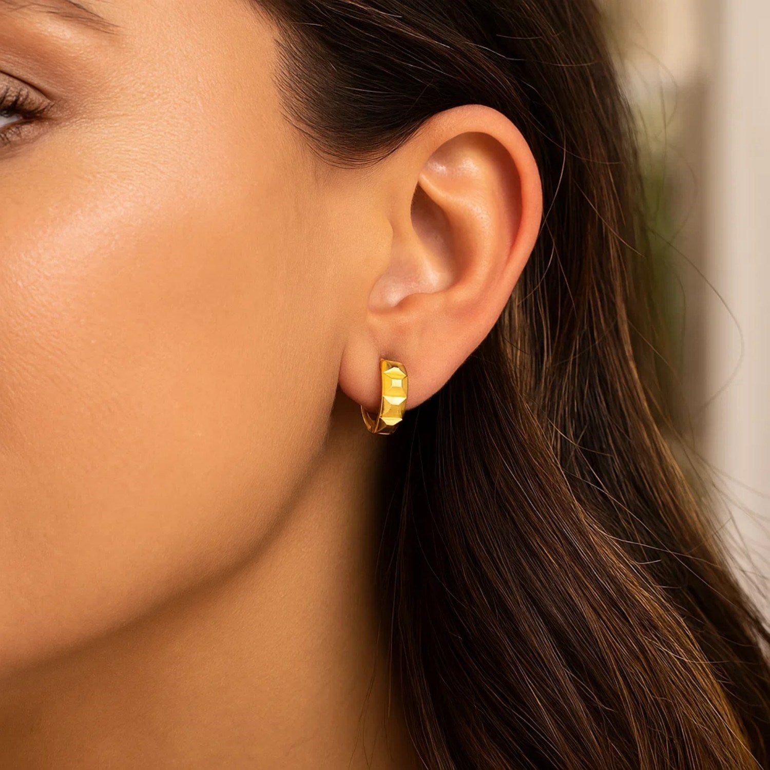 A woman wears 14K yellow gold J hoop earrings with a square faceted surface.