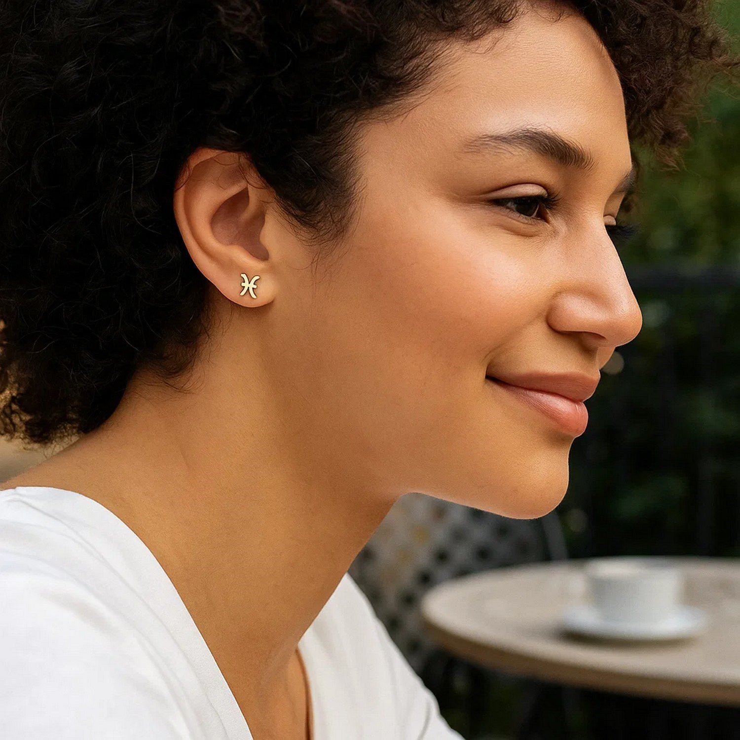 14K yellow gold Pisces stud earrings on a woman's ear.